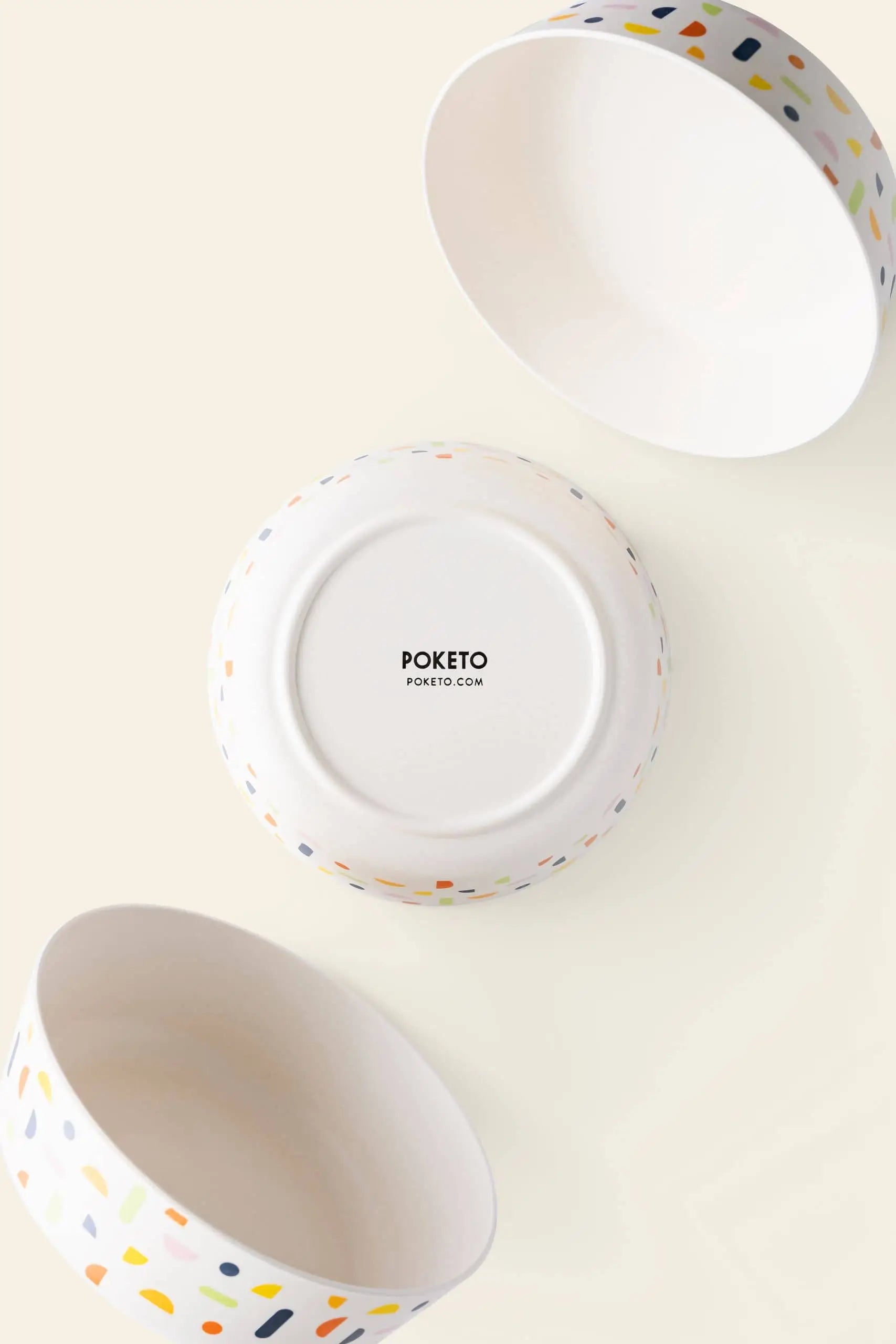 Three Poketo Bamboo Bowls in white ceramic with colorful terrazzo patterns are shown—two displaying their interiors and one upside down to reveal the Poketo brand name. Ideal for outdoor adventures, picnics, or pairing with any bamboo bowl set.