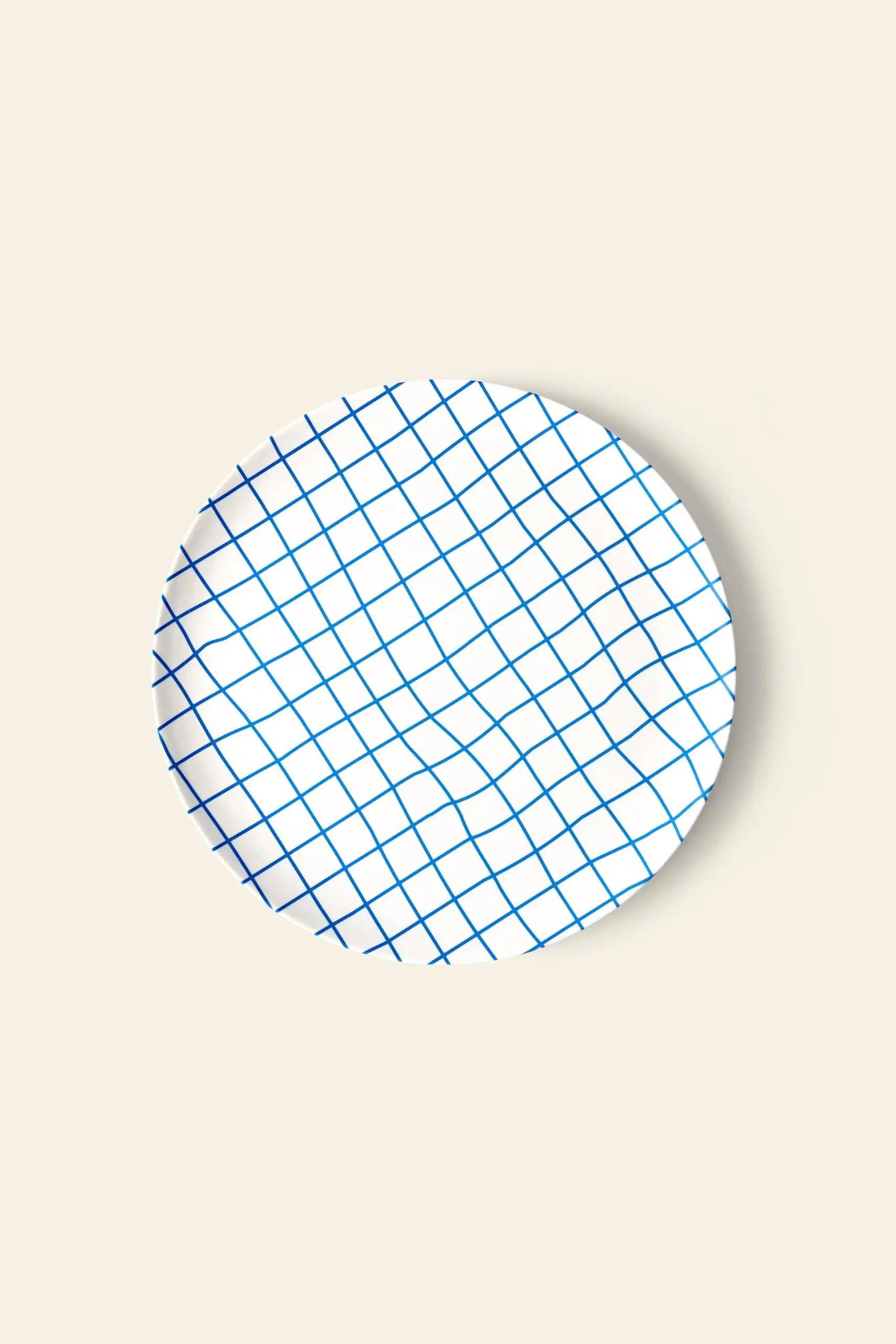 The Poketo Bamboo Dinner Plate by Poketo features a round white design with a blue crisscross grid, shown on a beige background—ideal for eco-friendly dinner parties.