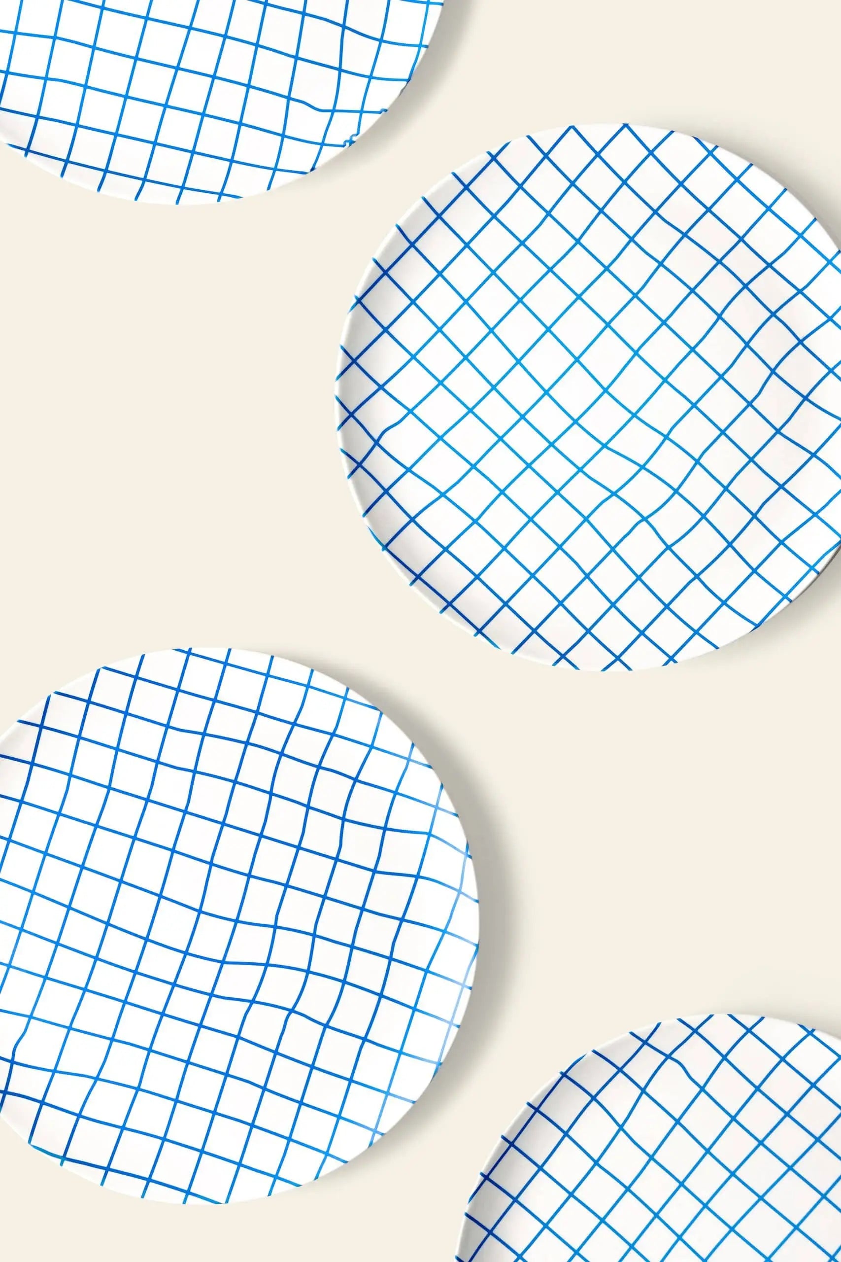 Four Poketo Bamboo Dinner Plates by Poketo, featuring a blue grid pattern, are arranged diagonally on a beige background with some plates extending past the edges—ideal for adding style to any dinner party.