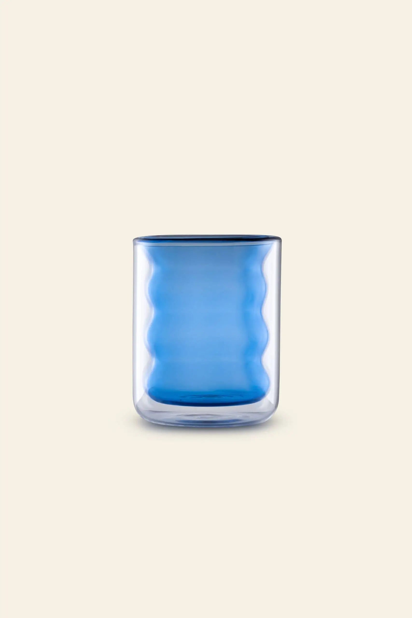 The Poketo Double Wall Groovy Cup by Poketo is hand-blown from borosilicate glass, featuring a wavy blue inner wall and set against a plain beige background.