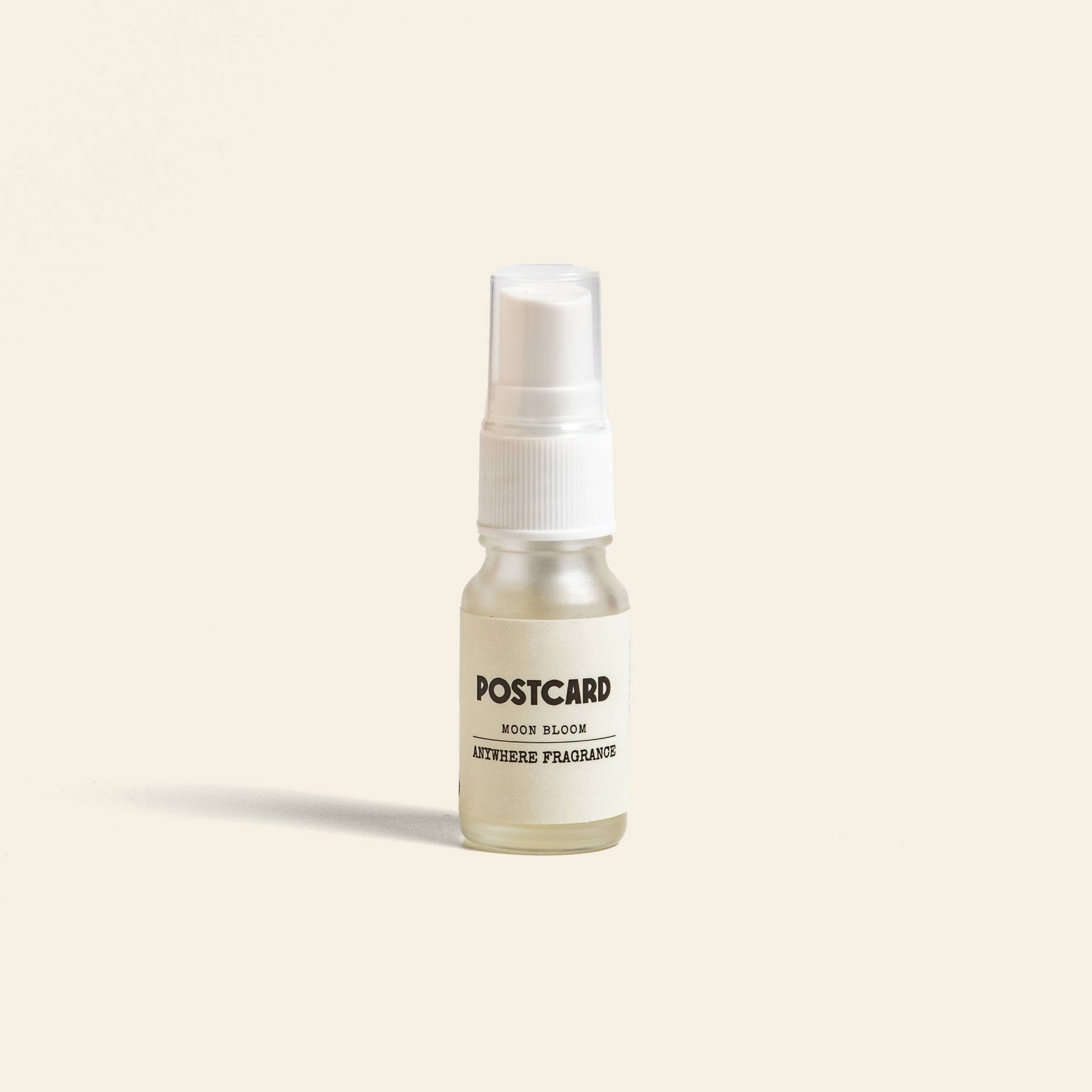 A small clear 10ml spray bottle of Postcard Anywhere Fragrance in Moon Bloom by Postcard sits against a light beige background, ready to share its unique and delicate scent.