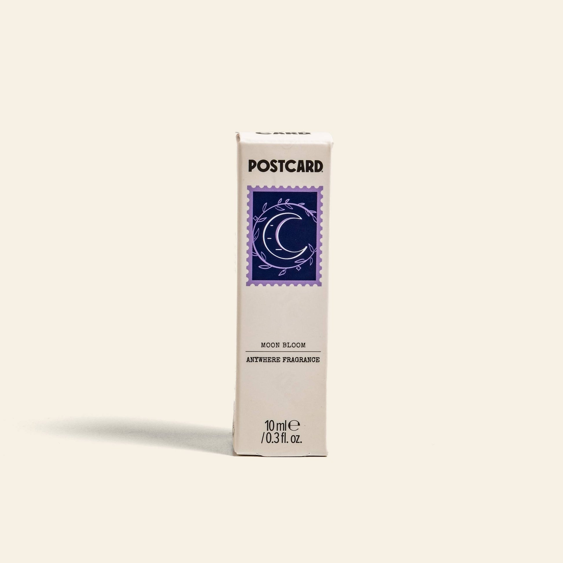 A rectangular white box from Postcard, labeled Moon Bloom Anywhere Fragrance, showcases a purple crescent moon with stars. Scent notes are highlighted, and 10ml (0.3 fl. oz) appears at the bottom.