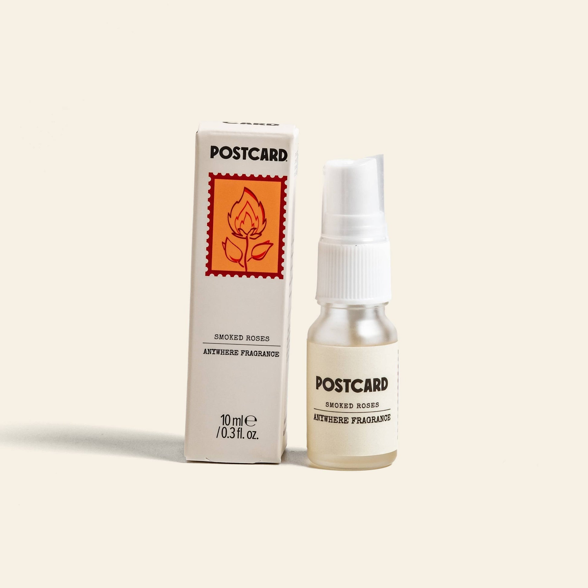 A 10ml Postcard Anywhere Fragrance in Smoked Roses stands by its box, which shows a rose with a flame. This Postcard scent blends rich rose and warm amber.
