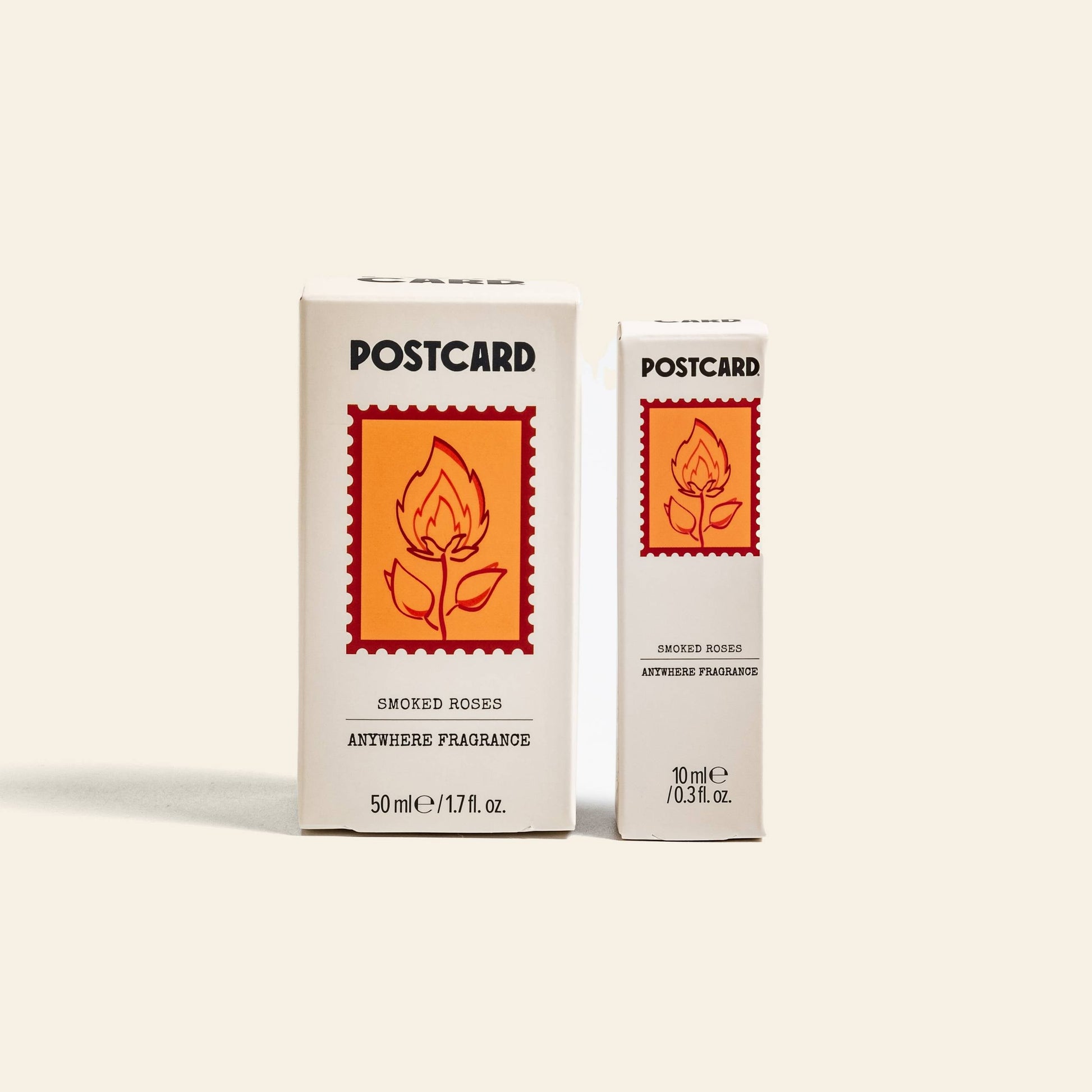 Two white boxes of Postcard Anywhere Fragrance, Smoked Roses (50 ml and 10 ml), each with a red-orange floral design—capturing notes of rose and warm amber. Brand: Postcard.