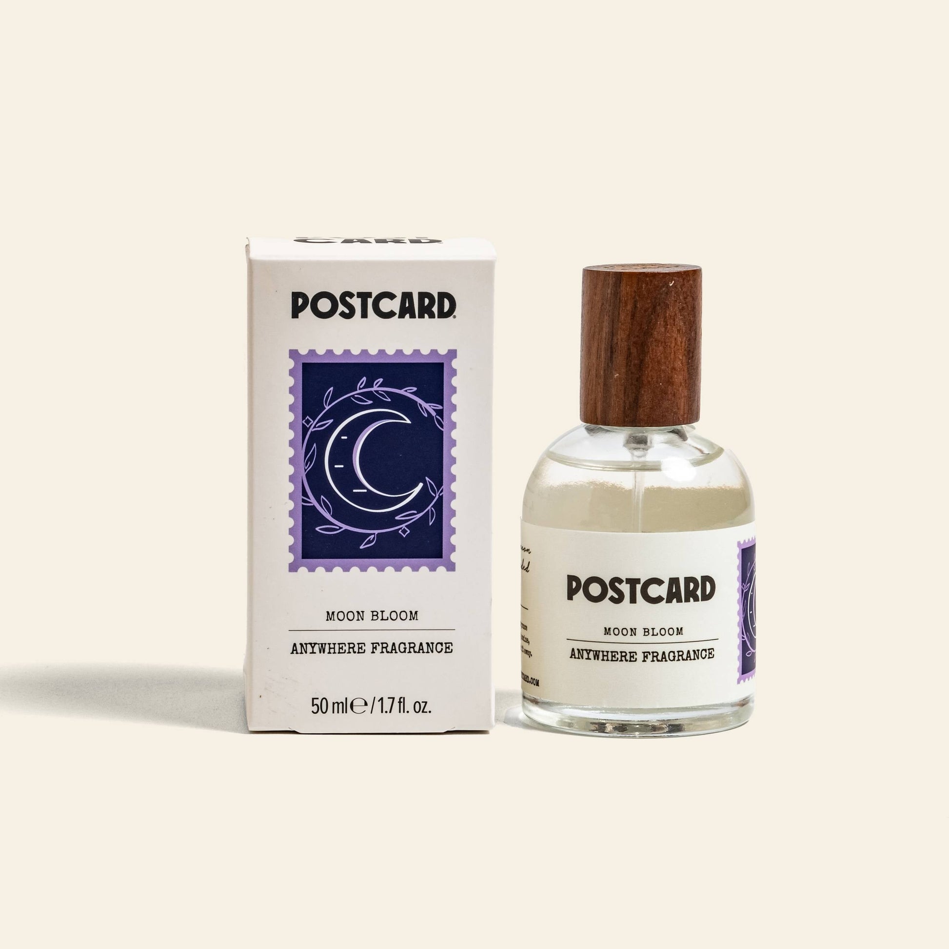 A 50ml Postcard Anywhere Fragrance in Moon Bloom stands by its white box, each accented with a wooden cap and purple crescent moon floral label—experience the brand’s captivating scent notes in this elegant bottle.