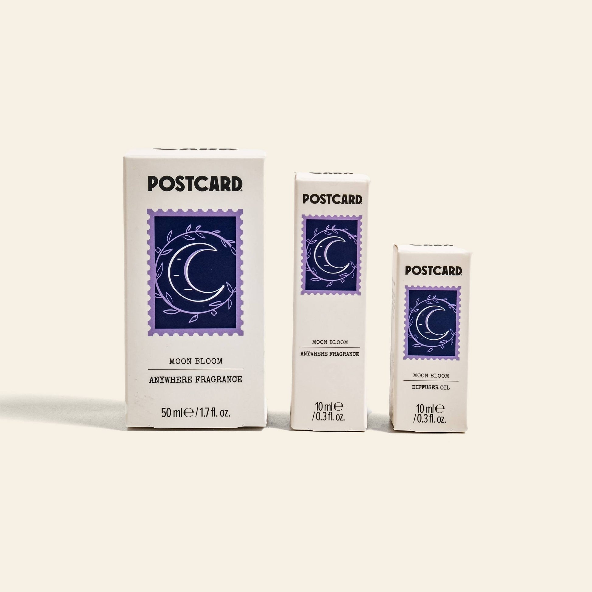 Three white boxes of Postcard Anywhere Fragrance, Moon Bloom scent (one 50ml, two 10ml), stand upright. Each features a purple crescent moon with stars—ideal for enjoying your favorite fragrance on the go.
