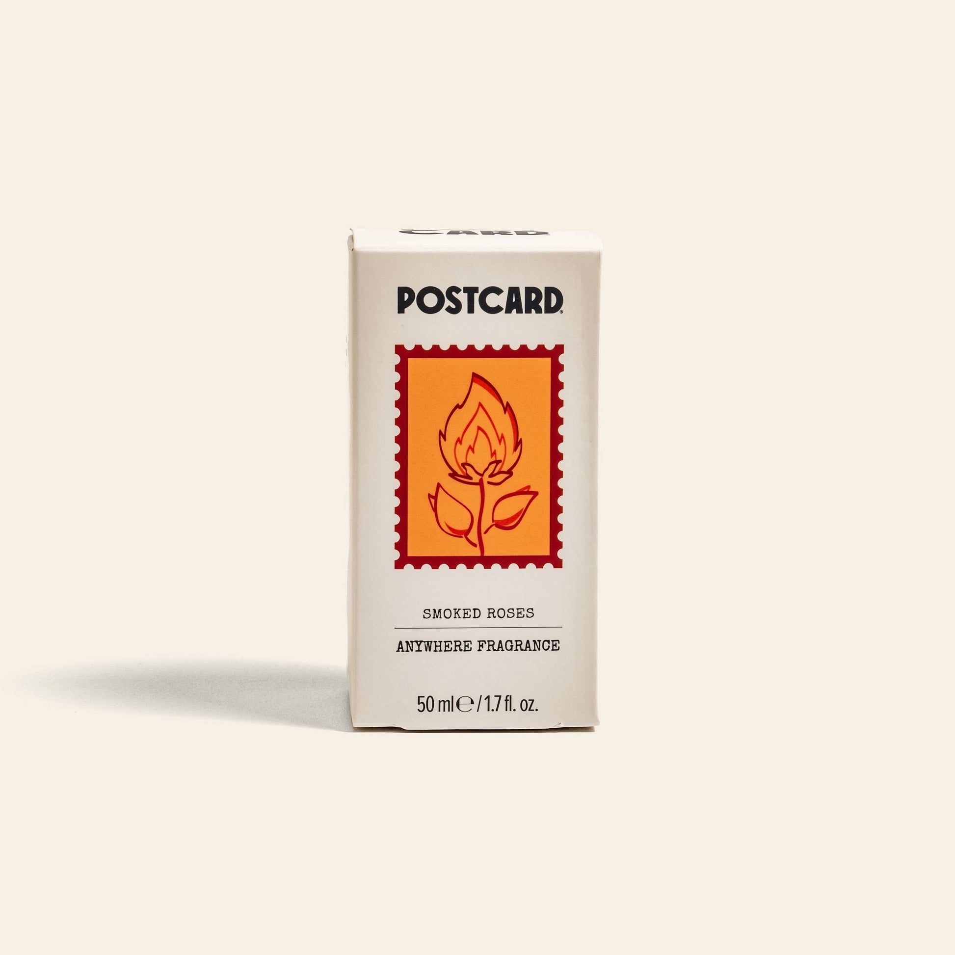 A beige box labeled Postcard Anywhere Fragrance, 50ml - Smoked Roses by Postcard features an orange stamp with a flaming rose and delivers amber fragrance with smoky rose perfume notes.