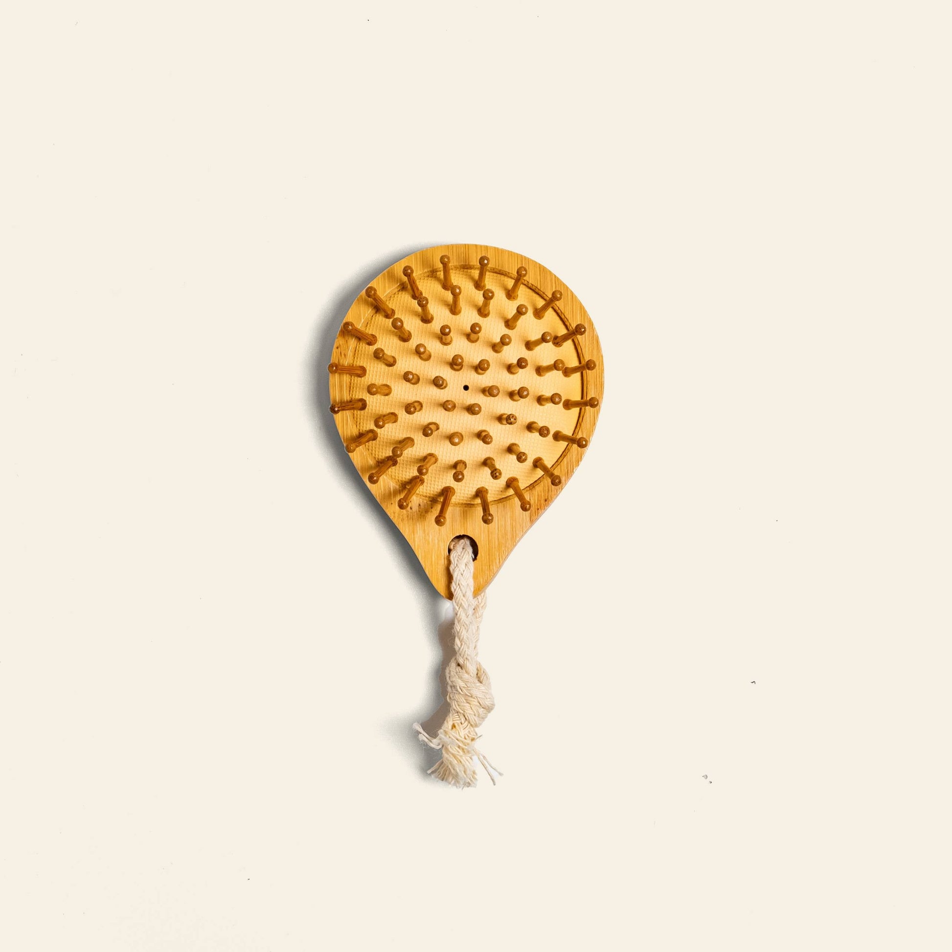 The Postcard Bamboo Scalp Massager Brush - Natural by Postcard features rounded bristles and a looped rope handle—ideal for promoting healthier hair growth. Shown on a plain light background.