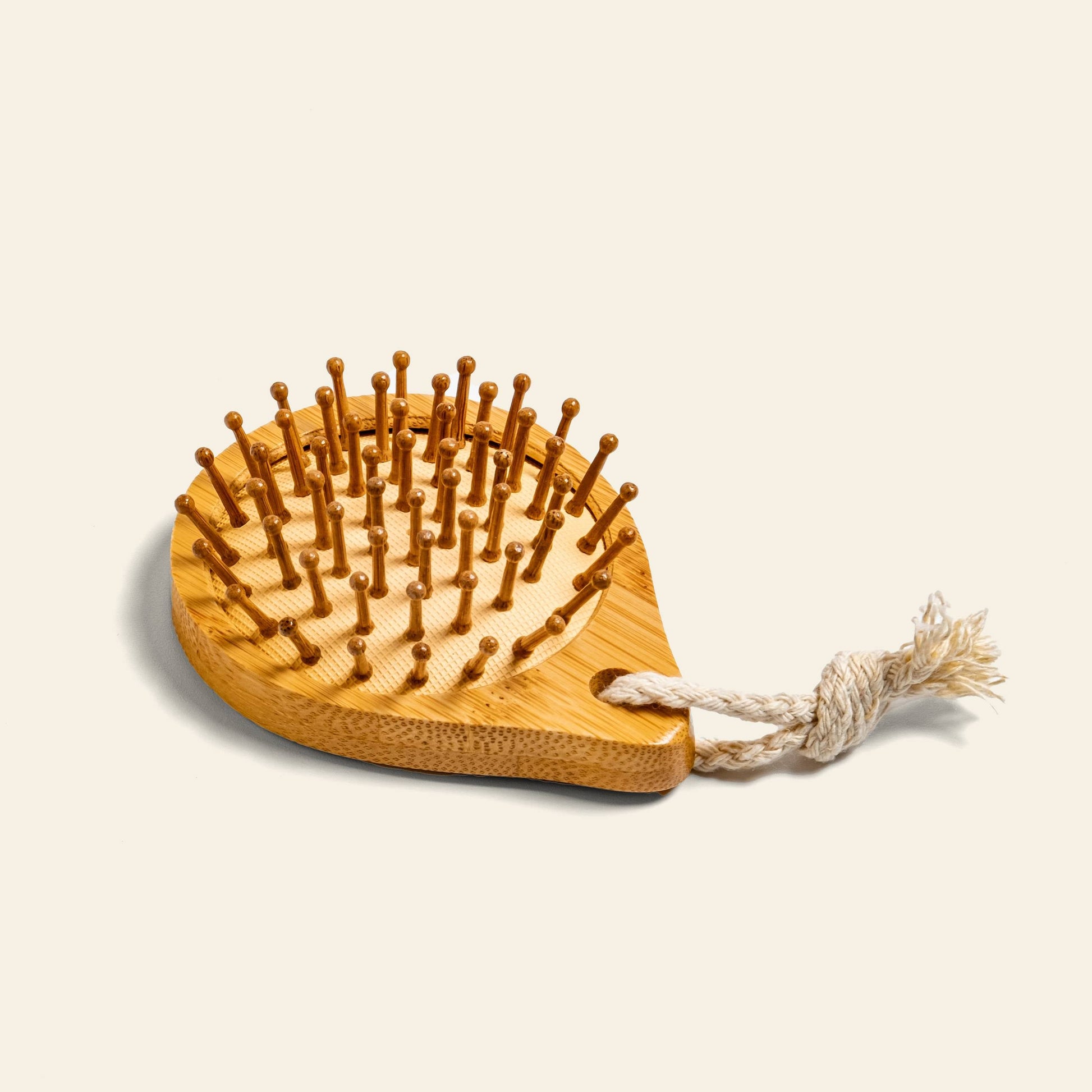 The Postcard Bamboo Scalp Massager Brush - Natural by Postcard features rounded bristles and a braided rope loop, displayed on a light beige background—ideal for promoting healthier hair growth.