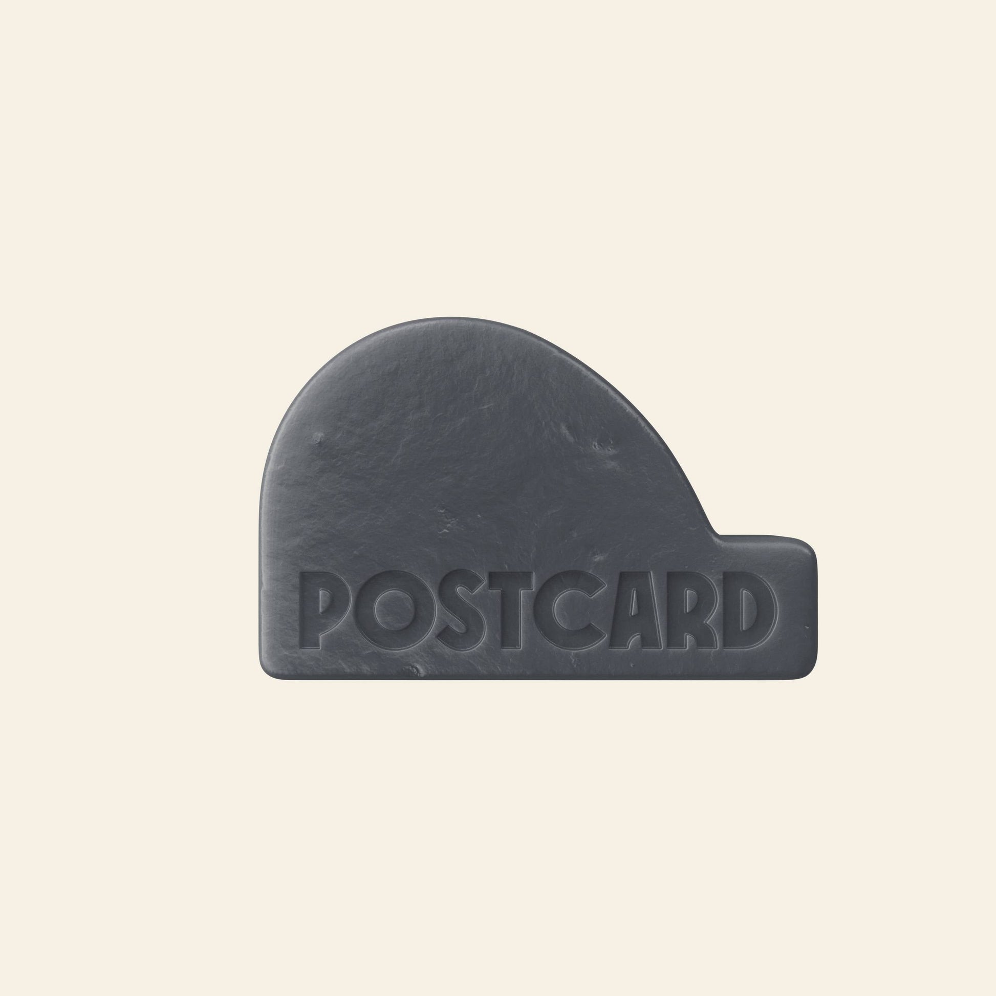 The Postcard Head-To-Toe Bar, 100g - Icy Peaks by Postcard is a black, rounded rectangular bar with an arched left side and the word POSTCARD embossed on it. Made with activated charcoal, its shown against a simple light beige background.