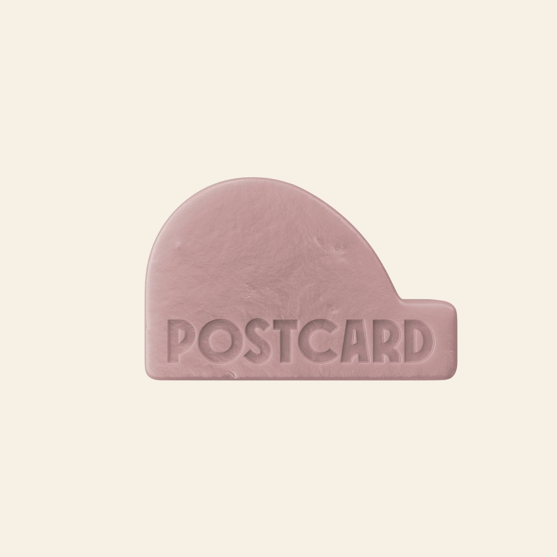 The Postcard Head-To-Toe Bar, 100g - Wild Flowers is a pink, rounded rectangular moisturizing cleansing bar embossed with POSTCARD, featuring a sulfate-free formula and shown against a plain cream background.