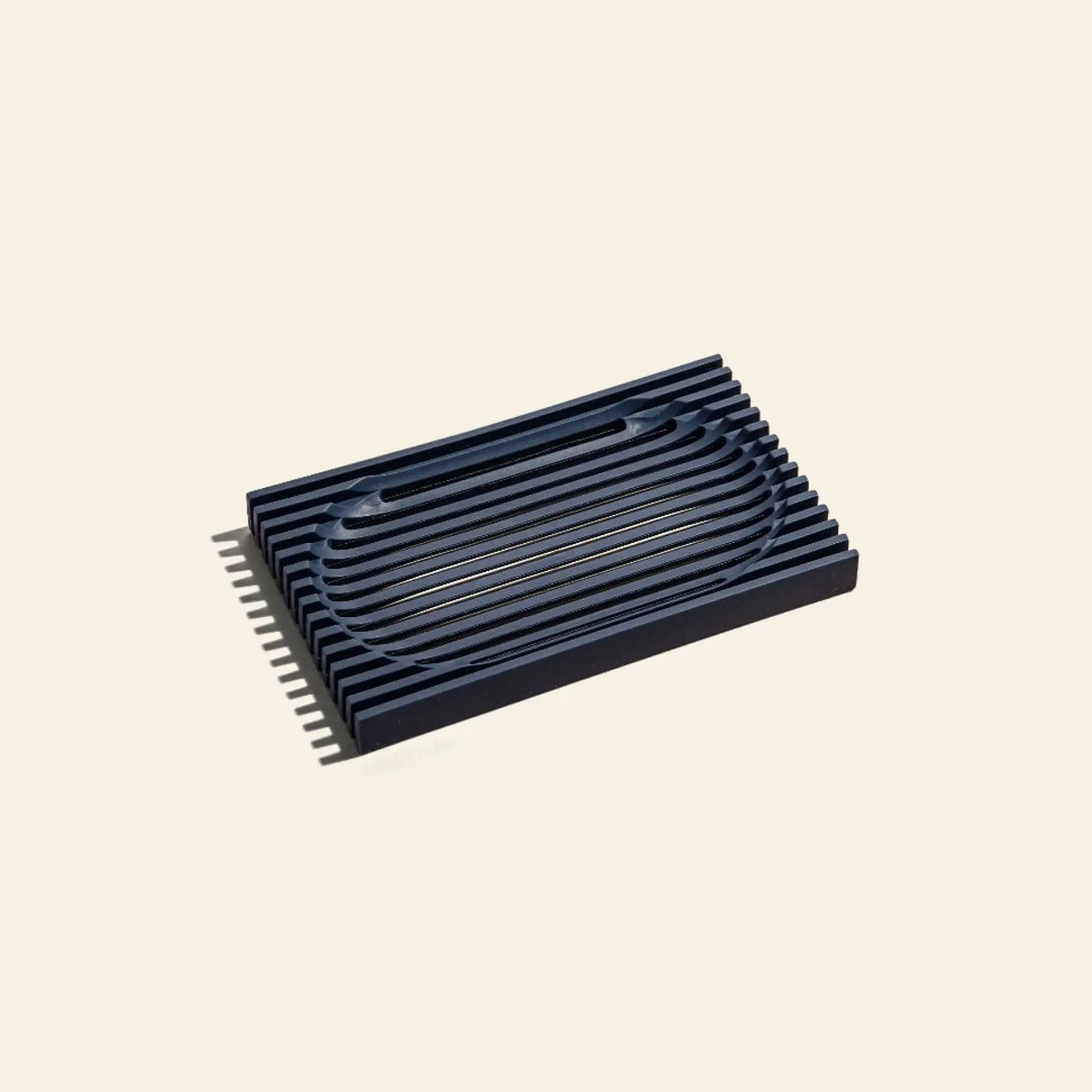 The Postcard Lattice Soap Dish by Postcard is a black, rectangular soap dish with ridged details and a modern minimalist design, crafted from recyclable resin and displayed against a plain beige background.