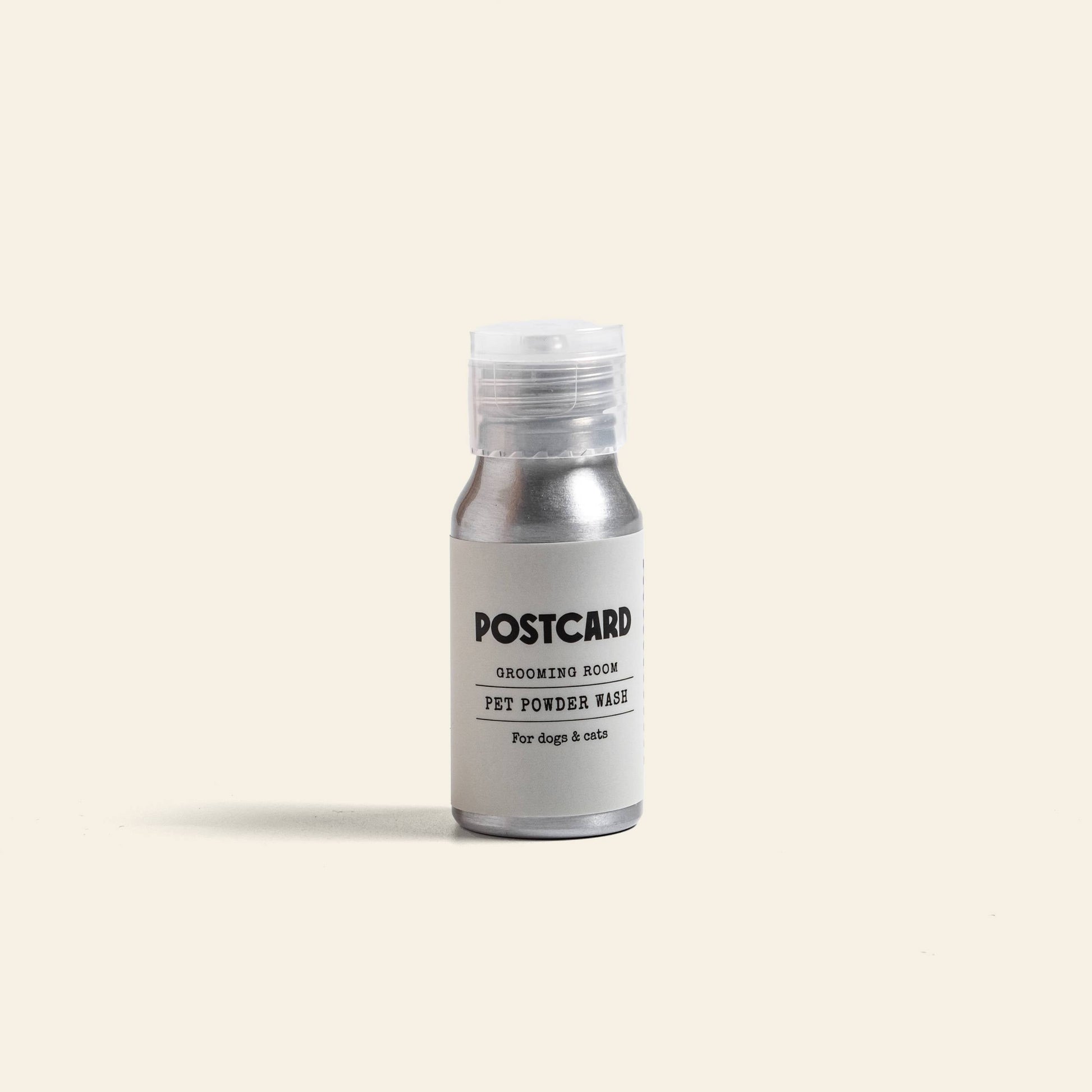 A small silver bottle of Postcard PET Powder Wash, 25g - Grooming Room, a sulfate-free powder-to-foam cleanser for dogs and cats, sits against a light beige background—ideal for your pet’s grooming routine.