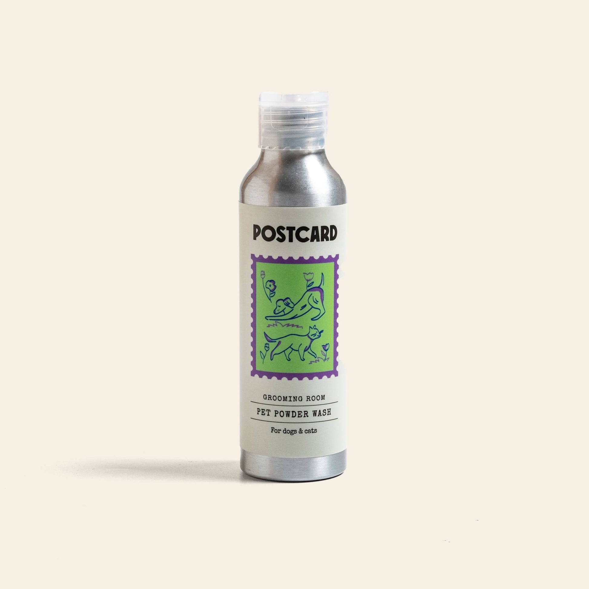 A silver Postcard PET Powder Wash bottle (80g) features a purple and green dog-and-cat illustration. Labeled Grooming Room, it’s a sulfate-free powder-to-foam cleanser for dogs & cats, shown upright against a plain background.
