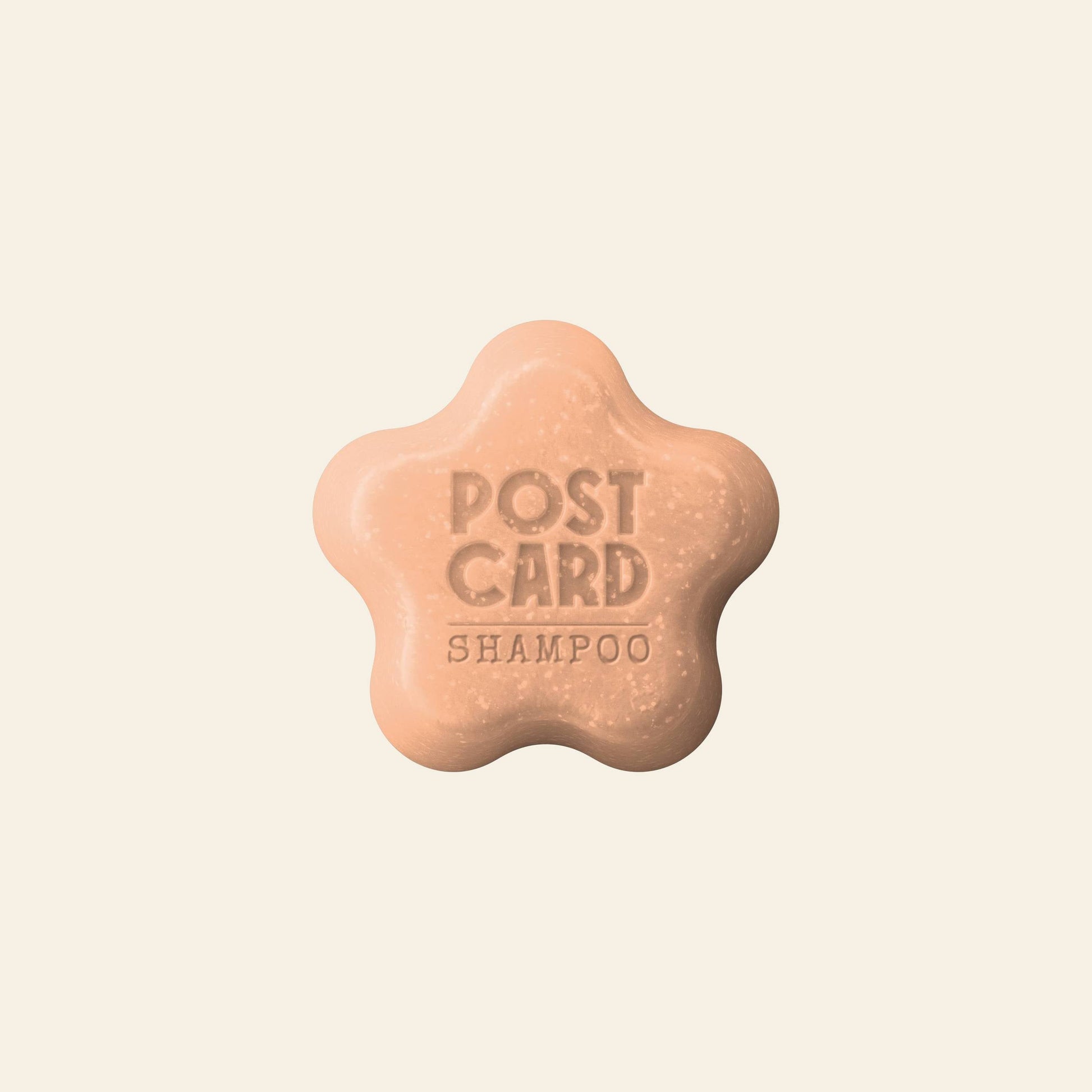 A beige, flower-shaped Postcard Shampoo Bar (60g - Citrus Circus) with POSTCARD SHAMPOO engraved on top, vitamin C-rich and sulfate-free, is set against a plain, light background. Brand: Postcard.
