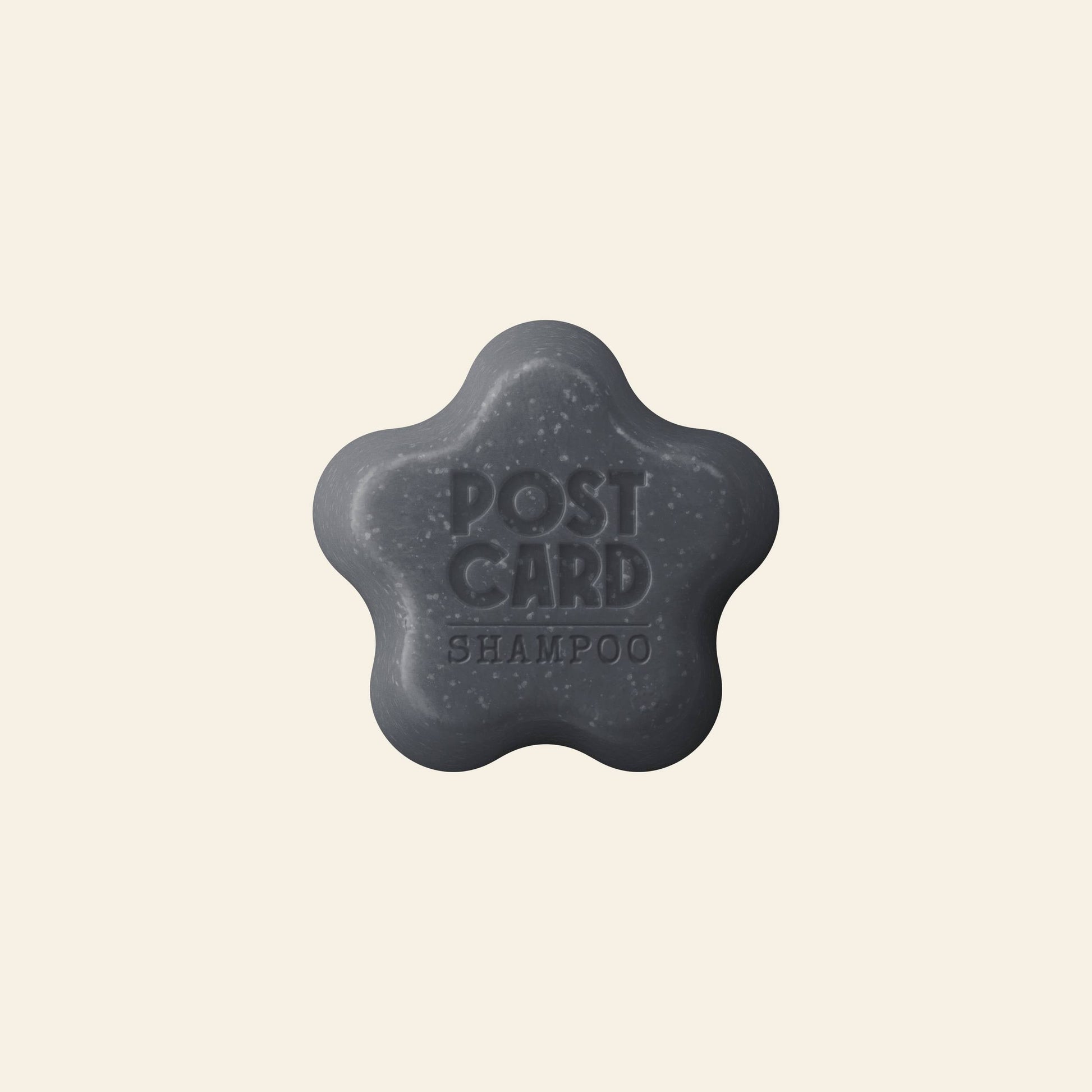 The Postcard Shampoo Bar, 60g - Icy Peaks, is a dark gray flower-shaped bar with activated charcoal for oily hair, embossed with POSTCARD SHAMPOO and displayed on a light beige background.
