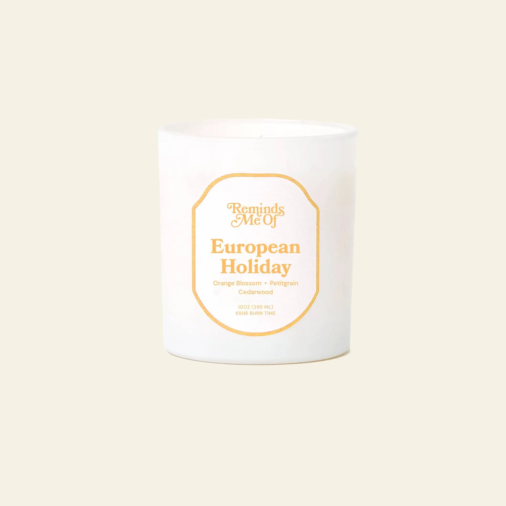 The Reminds Me Of European Holiday Candle (10oz) by Reminds Me Of is a white candle in a glass jar with notes of orange blossom, bergamot, pomegranate, and cedarwood, shown against a plain beige background.