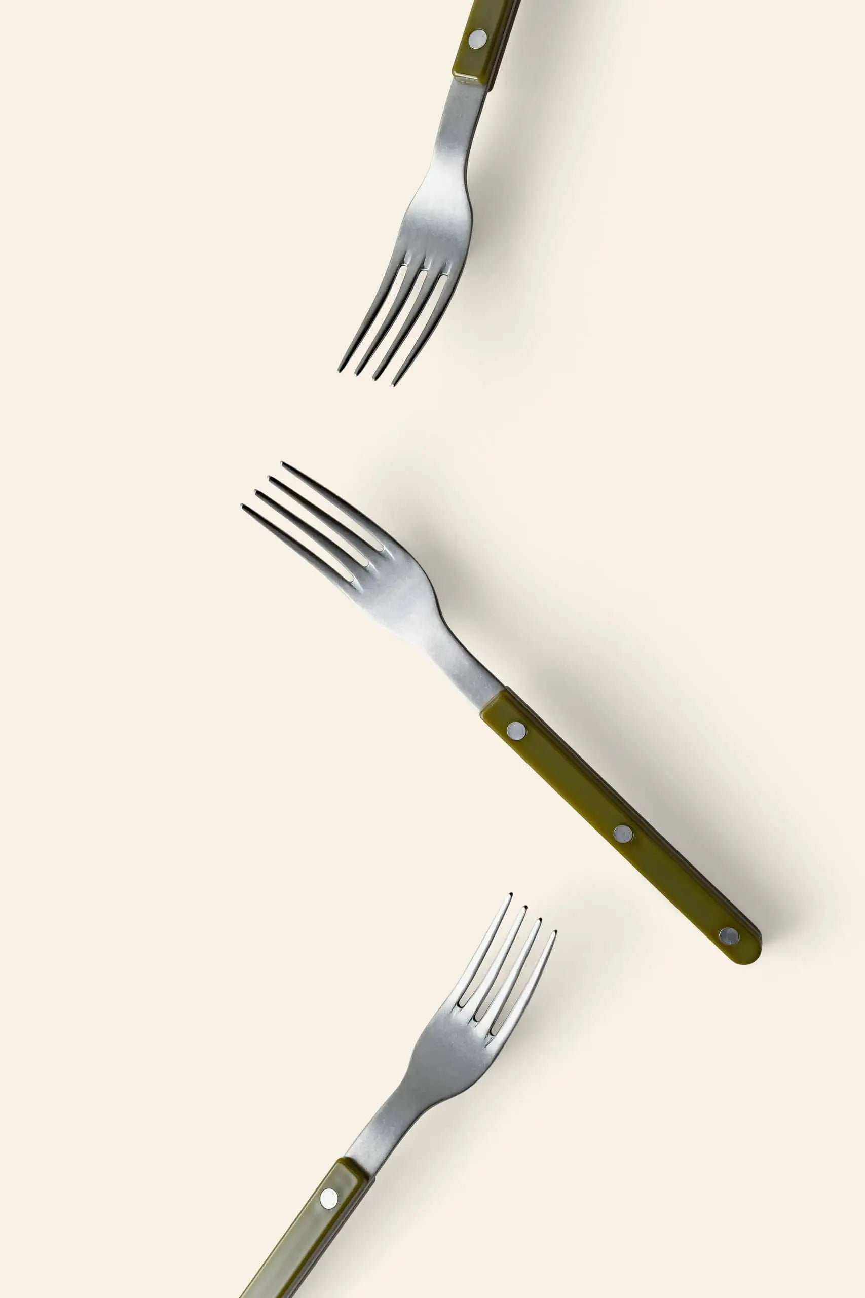 Three Sabre Bistrot Vintage Dinner Forks by Sabre, featuring green handles and stainless steel, are arranged diagonally on a light off-white background, each fork pointing in a different direction for a charming vintage look.