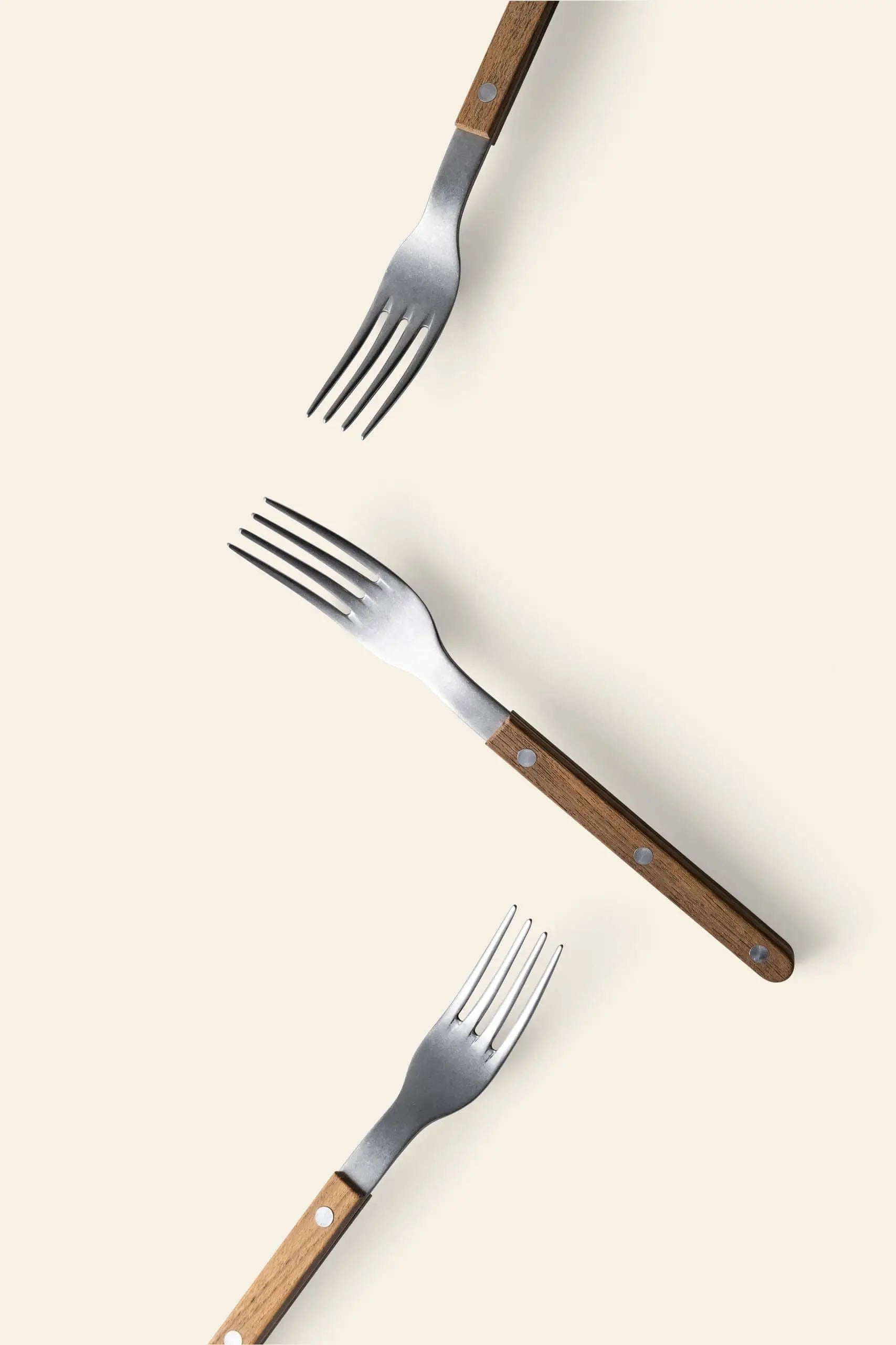 Three Sabre Bistrot Vintage Dinner Forks by Sabre, featuring brown wooden handles and stainless steel tines, are arranged diagonally on a light beige background, evenly spaced to create a charming vintage display.