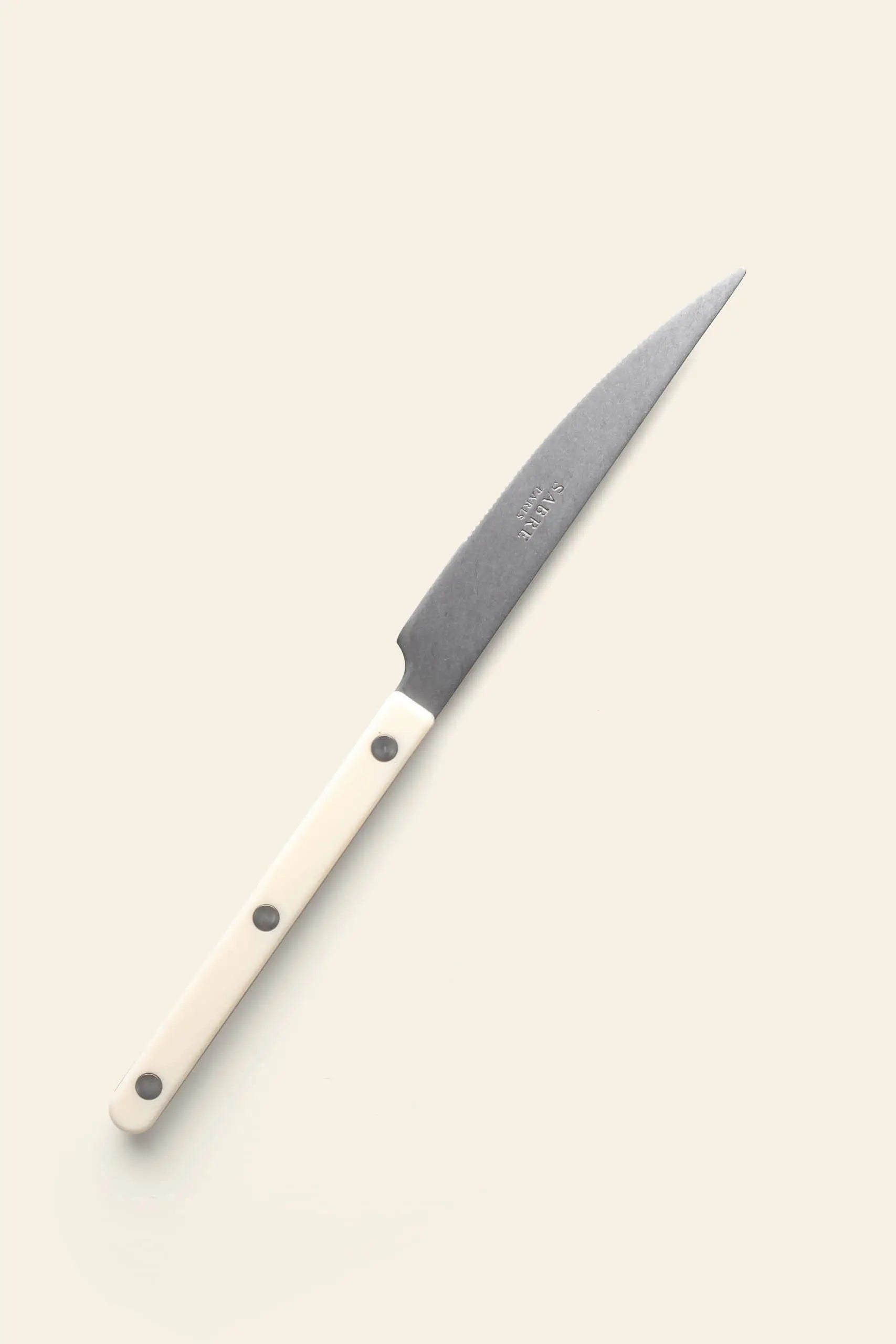 The Sabre Bistrot Vintage Dinner Knife by Sabre features a dark blade and white handle with three metal rivets, offering classic French bistrot style for your kitchen. Set against a plain light background, its both stylish and practical.