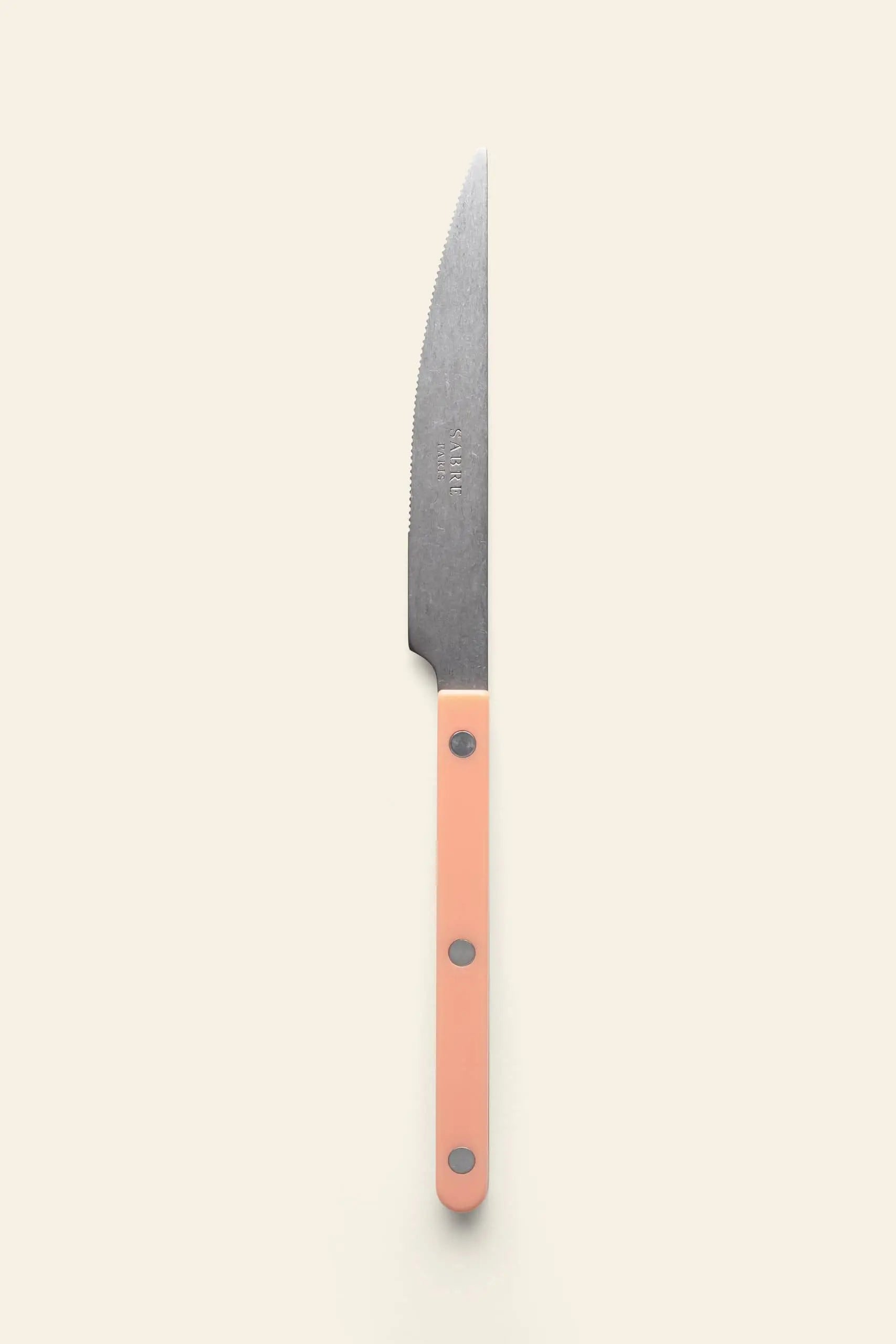 The Sabre Bistrot Vintage Dinner Knife by Sabre features a silver blade and light pink handle, displayed against a plain off-white background in classic French bistrot style.