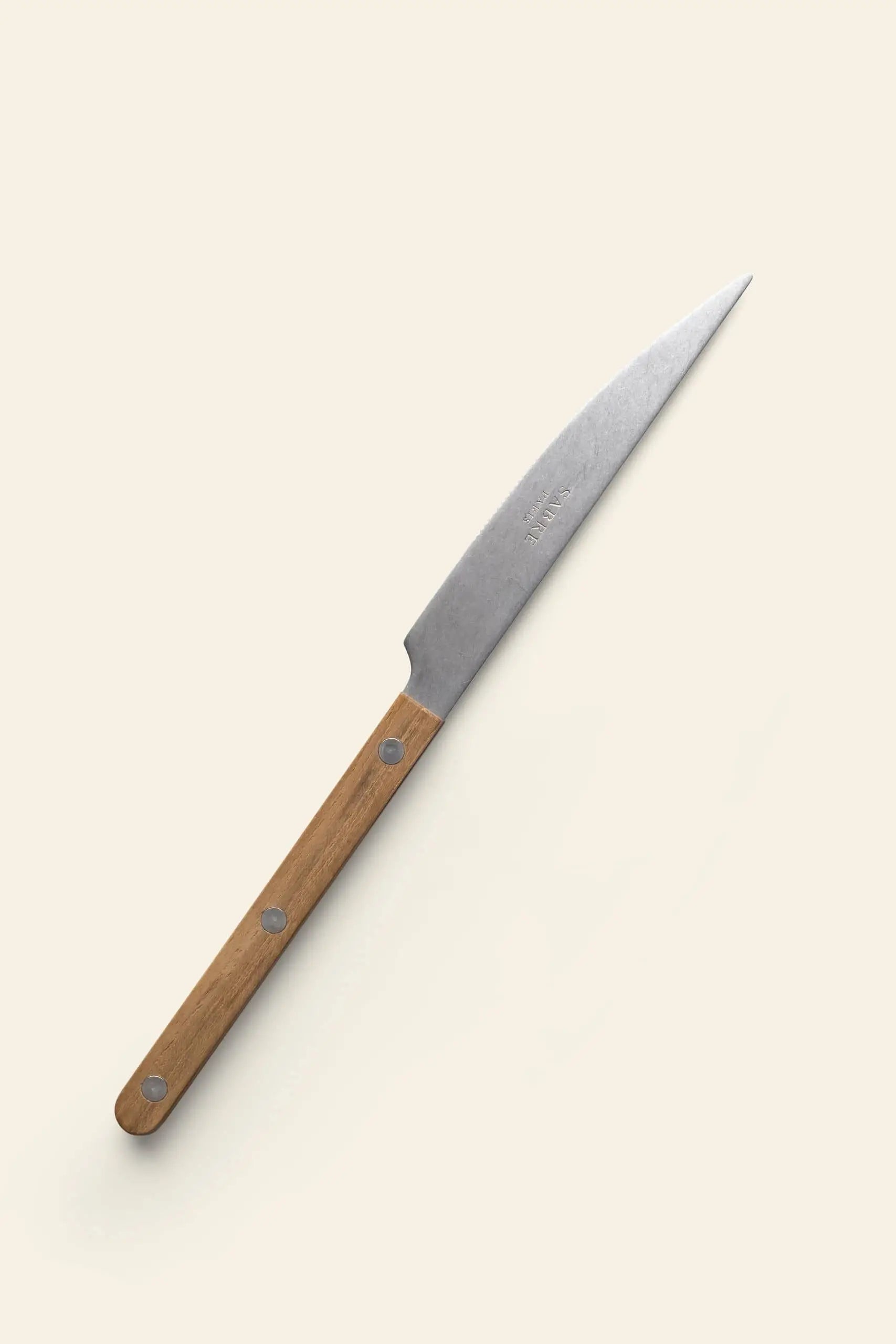 The Sabre Bistrot Vintage Dinner Knife by Sabre features a pointed stainless steel blade and a light brown wooden handle with three metal rivets, displayed on a light beige background and channeling classic French bistrot style.