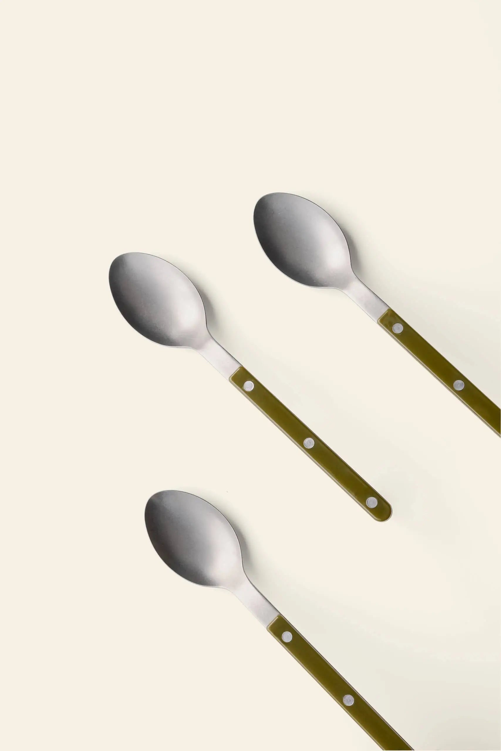 Three Sabre Bistrot Vintage Soup Spoons by Sabre, featuring green handles, are arranged diagonally in parallel lines on a plain, light background, evoking the charm of a French cafe.