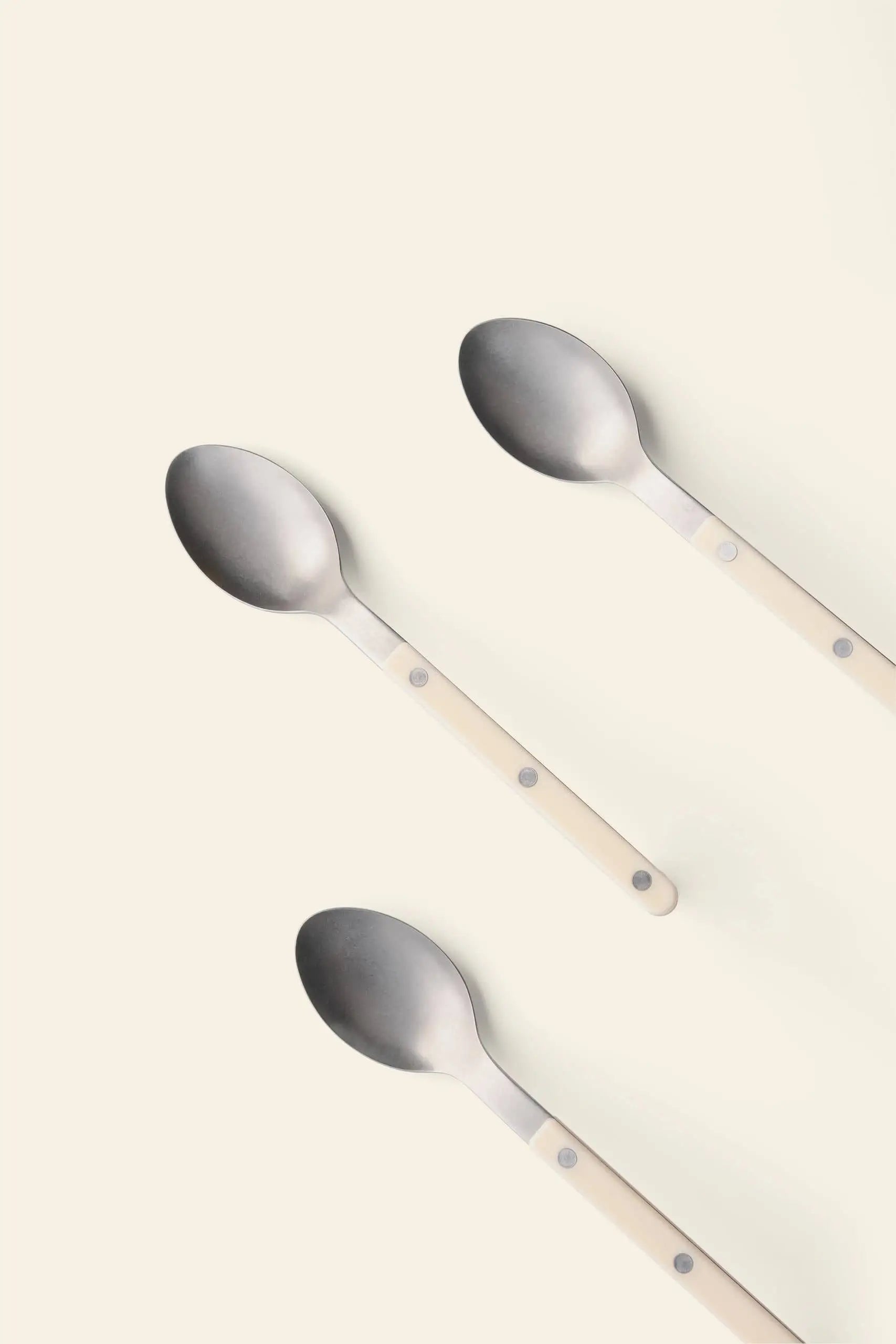 Three Sabre Bistrot Vintage Soup Spoons by Sabre, featuring cream-colored handles, are arranged diagonally on a light background, capturing the charm of a French cafe.
