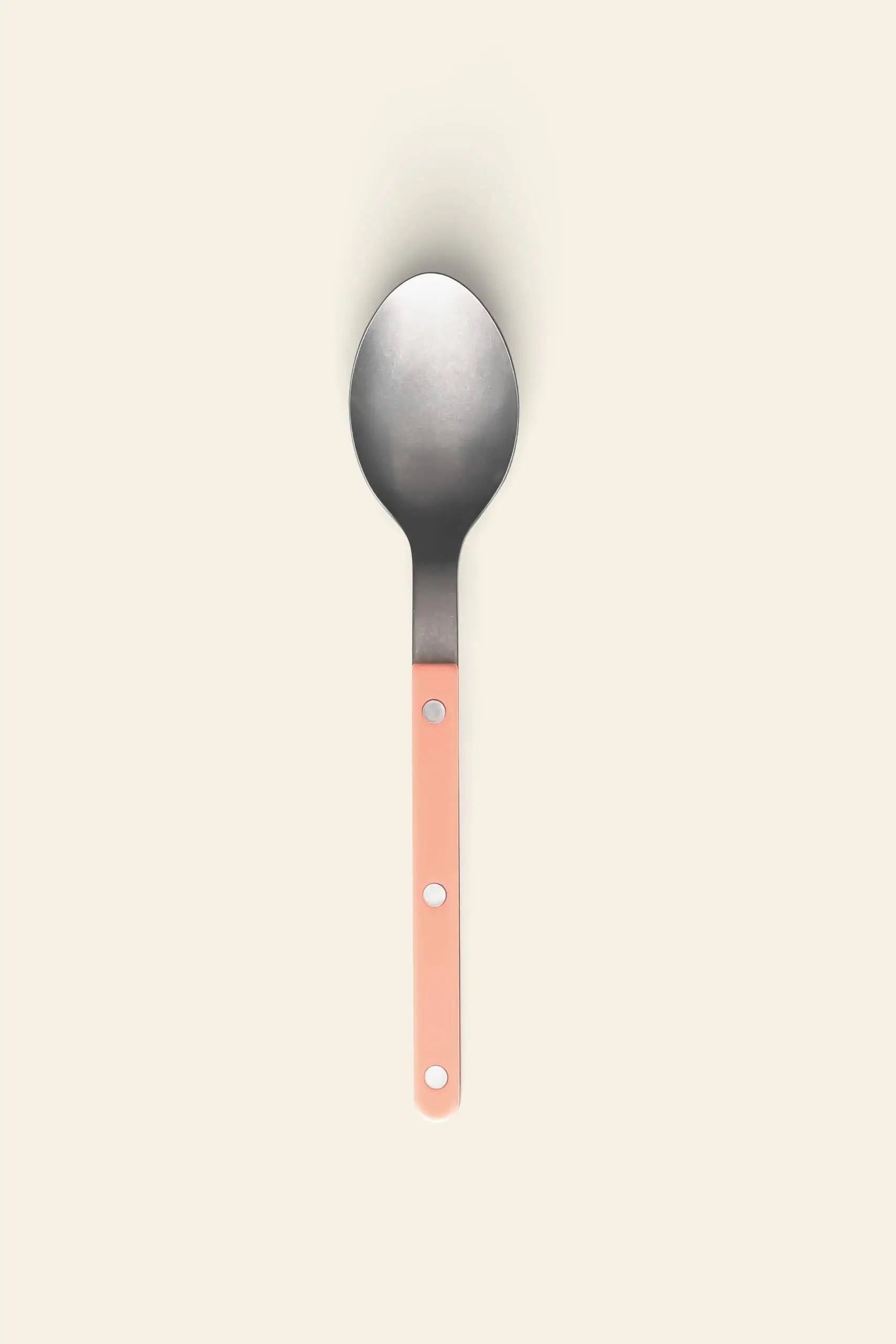 The Sabre Bistrot Vintage Soup Spoon by Sabre, featuring a pink handle with three circular holes, is centered on a plain, light beige background.