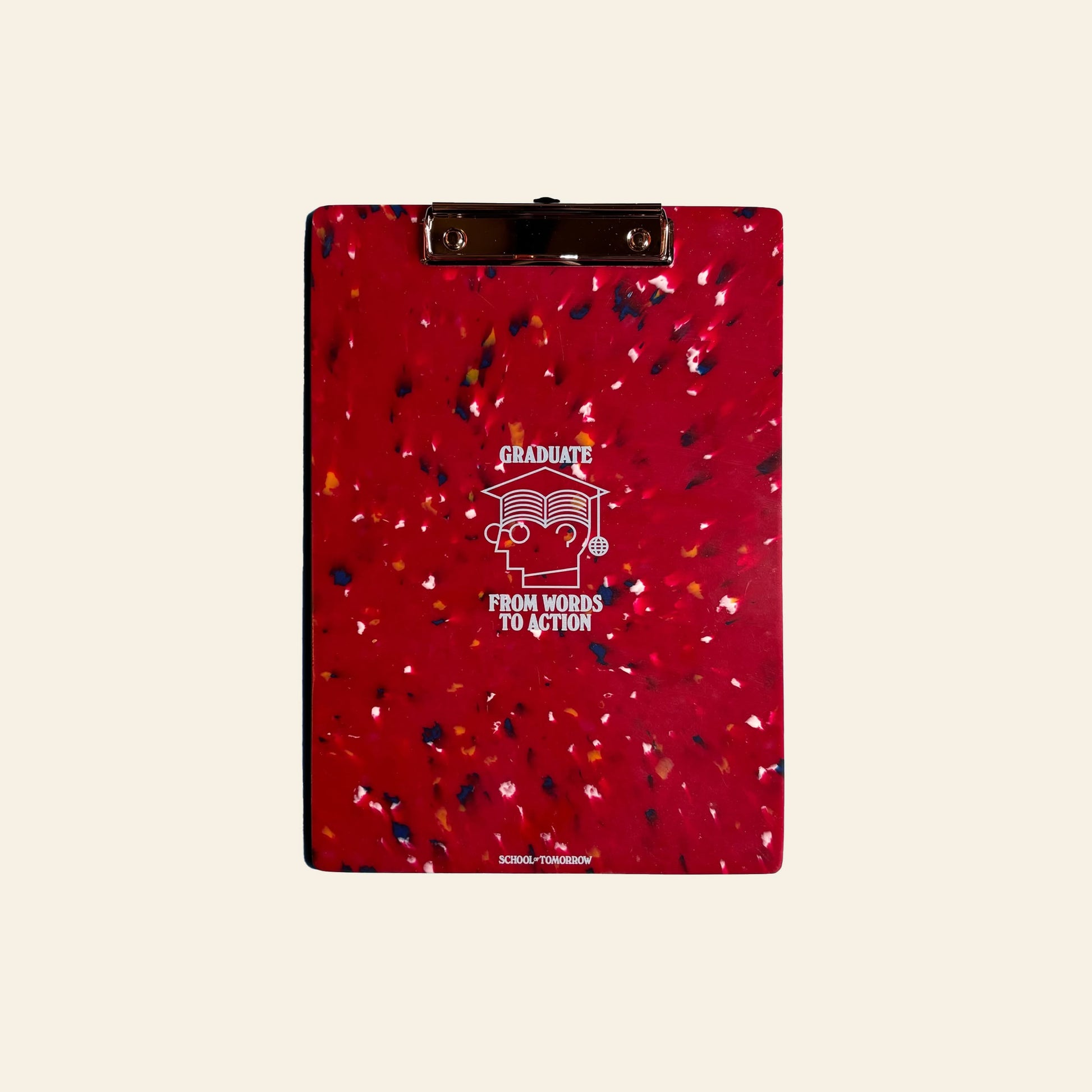 The School of Tomorrow A4 Clipboard - Red by School of Tomorrow is made from recycled bottle caps. It features colorful speckles, “GRADUATE FROM WORDS TO ACTION” in white above an open book, and sits on a plain beige background—eco-friendly for achievers.