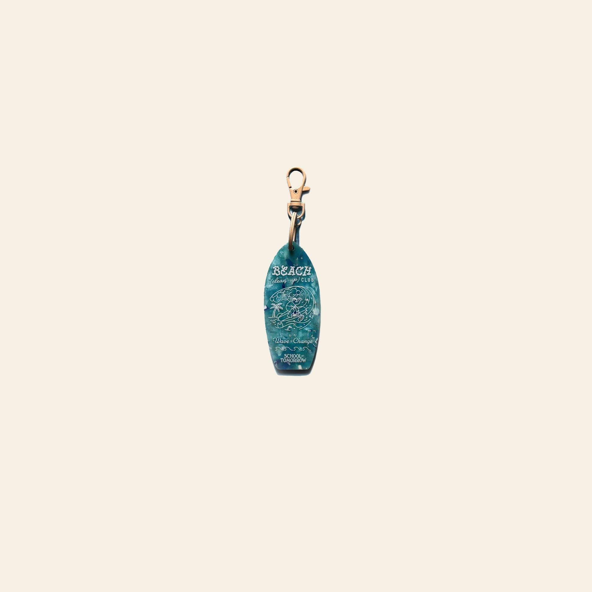 The School of Tomorrow Keychain - Blue by School of Tomorrow is a small surfboard-shaped keychain, handmade from repurposed plastic, with BEACH, an ocean wave design, and a gold clasp displayed on a plain beige background.