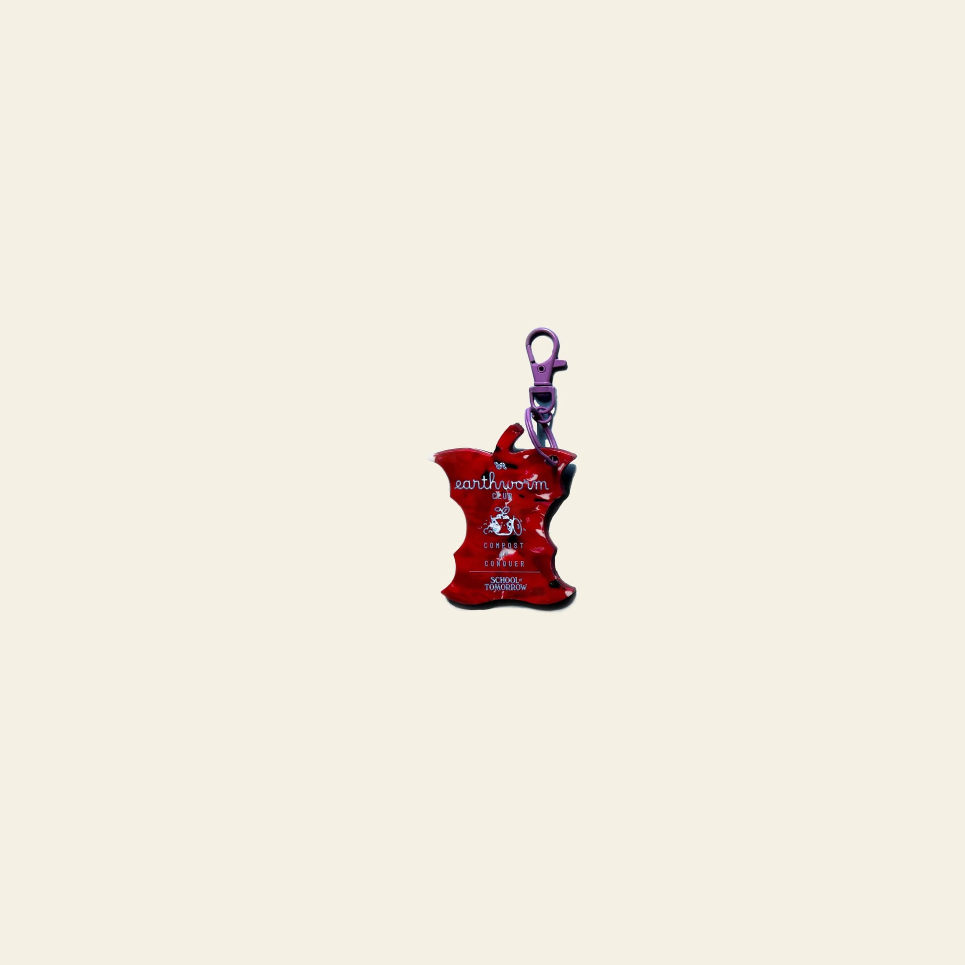 The School of Tomorrow Keychain - Red is an apple core-shaped handmade keychain with a purple clasp, white text, and a small front graphic—ideal for eco-conscious users. Displayed on a light beige background. Brand: School of Tomorrow.
