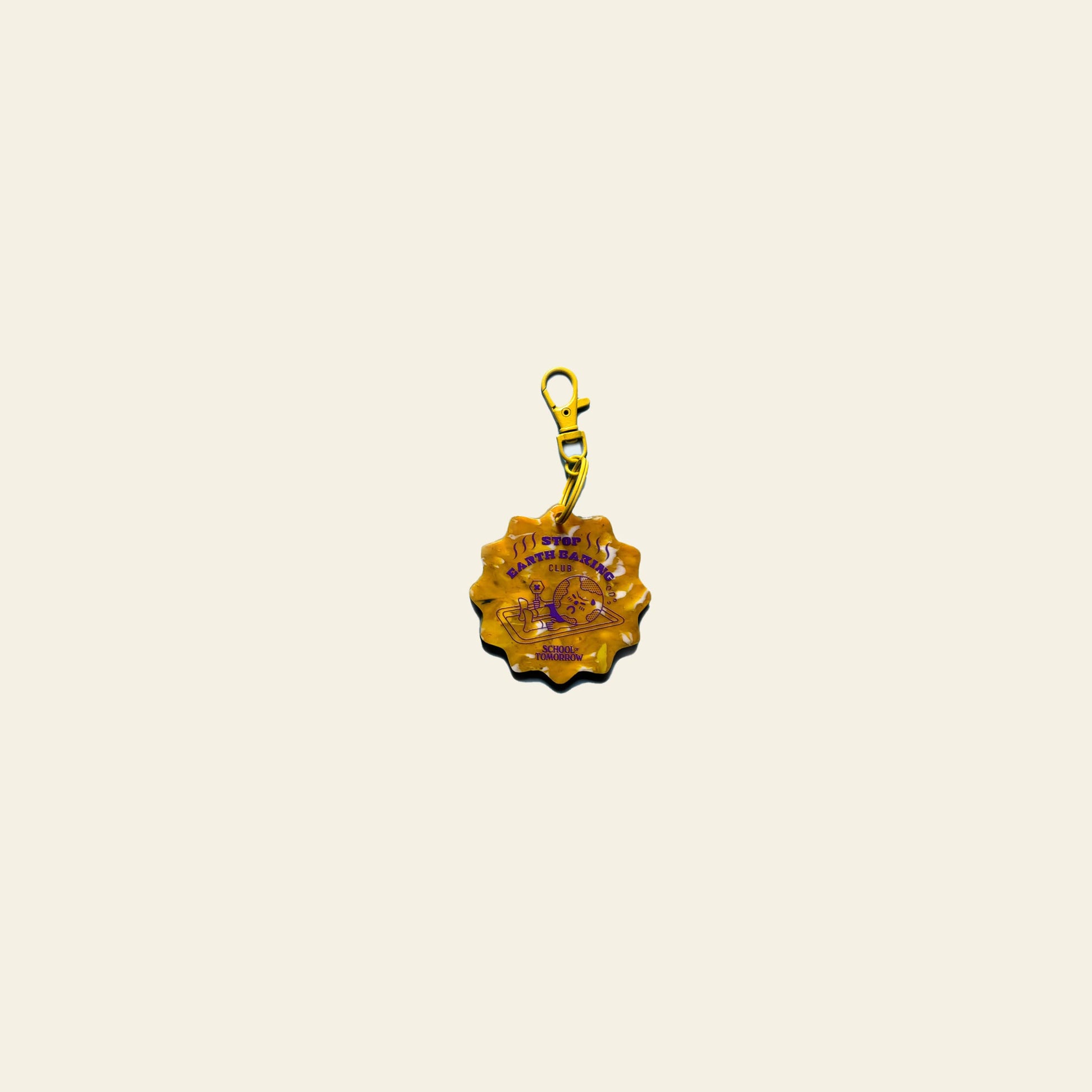 The School of Tomorrow Keychain - Yellow by School of Tomorrow features a scalloped edge, purple text, and design, with a matching clip, displayed centered on a plain cream background.