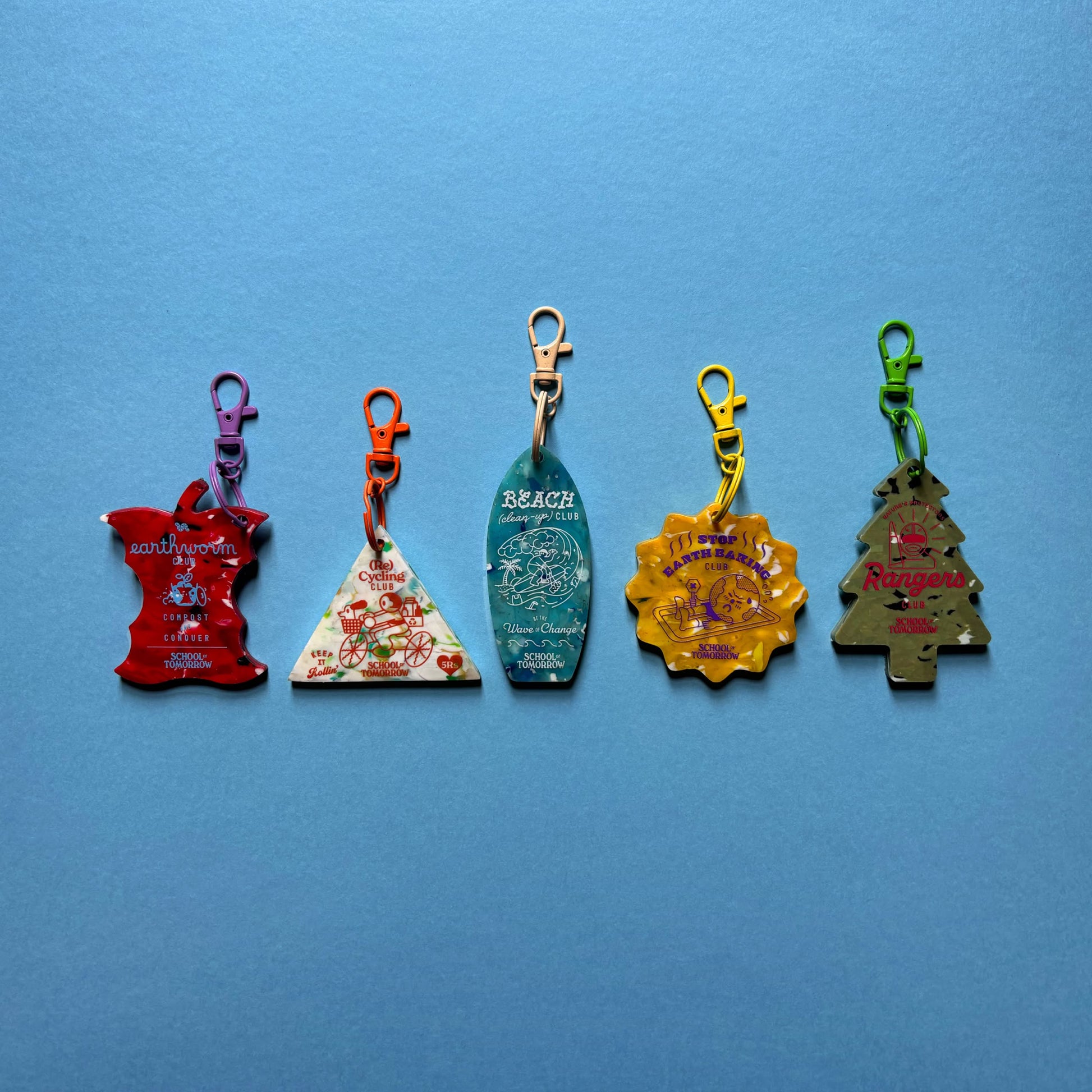 The School of Tomorrow Keychain - Yellow by School of Tomorrow is a sustainable, handmade accessory with a unique printed design and metal clip, photographed on a blue background.