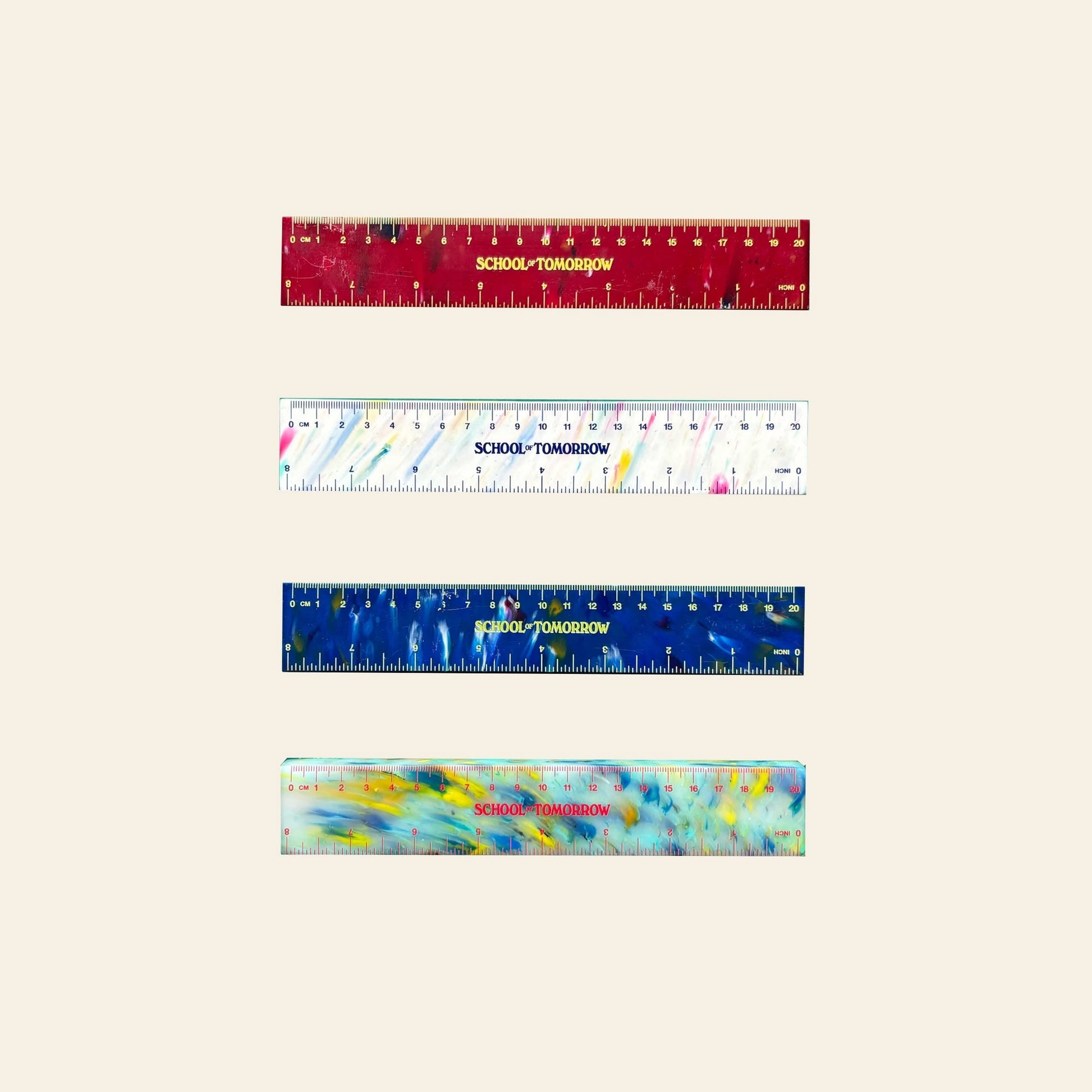 Four vibrant SCHOOL TOMORROW 20cm thick rulers—red, white, blue, and multicolored—by School of Tomorrow are stacked vertically on beige, combining eco-friendly HDPE plastic waste into unique math instruments.