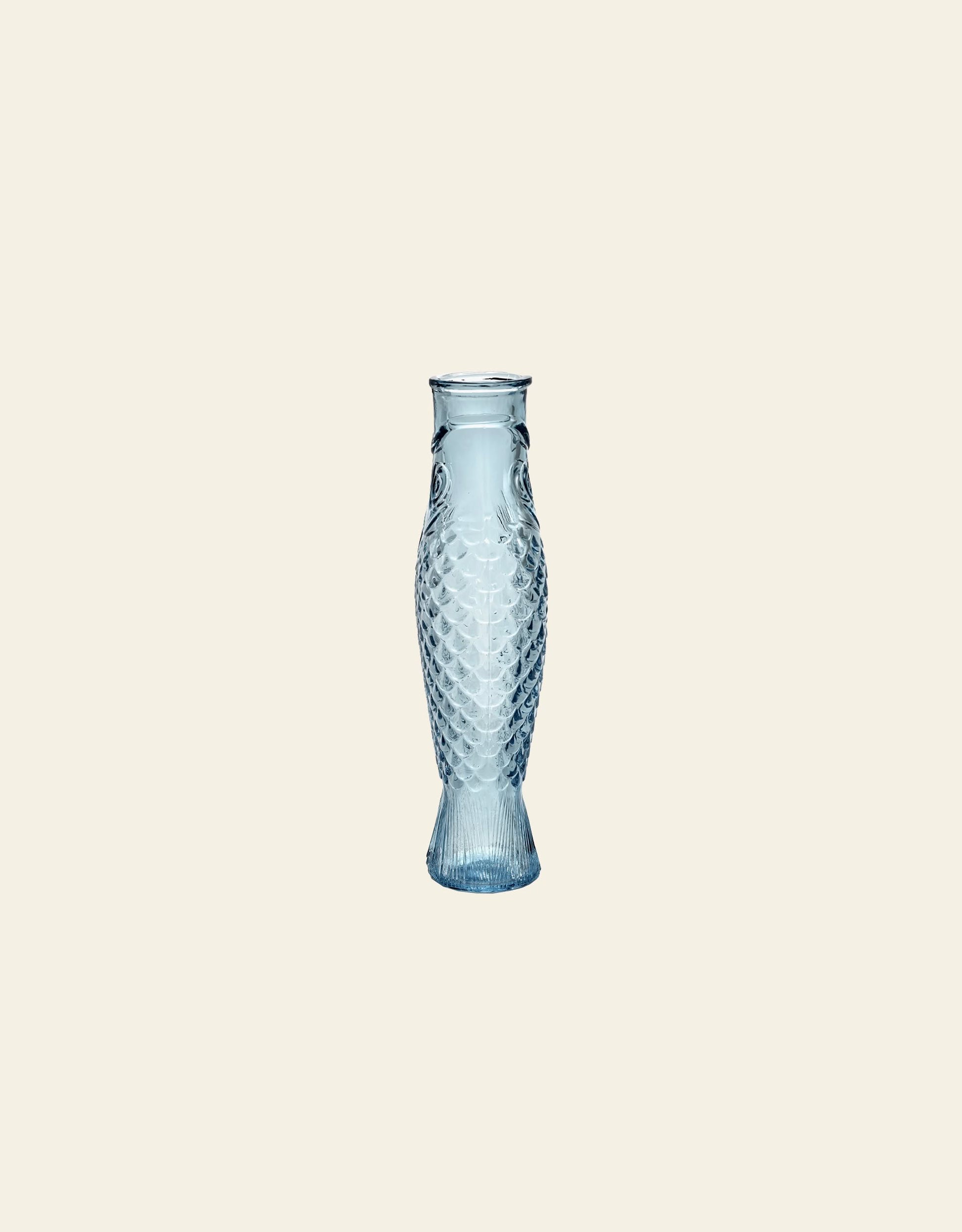 The Serax Fish & Fish Carafe by Serax, featuring blue glass with a fish-scale pattern and a flared base, is showcased centered on a plain light beige background.