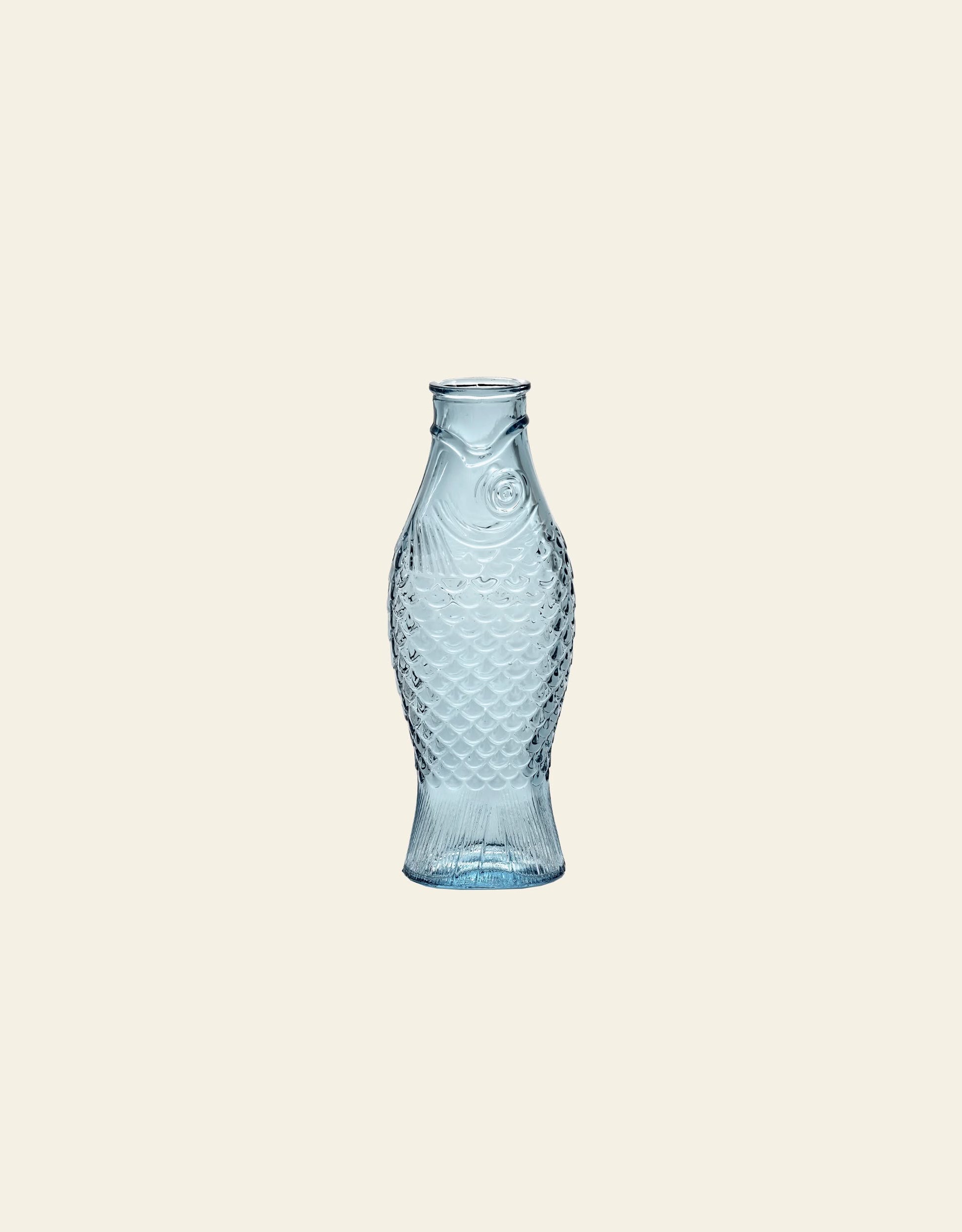 The Serax Fish & Fish Carafe by Serax features detailed scales and fins in clear blue glass, standing upright for a striking look—an eye-catching piece to enhance your tableware collection.