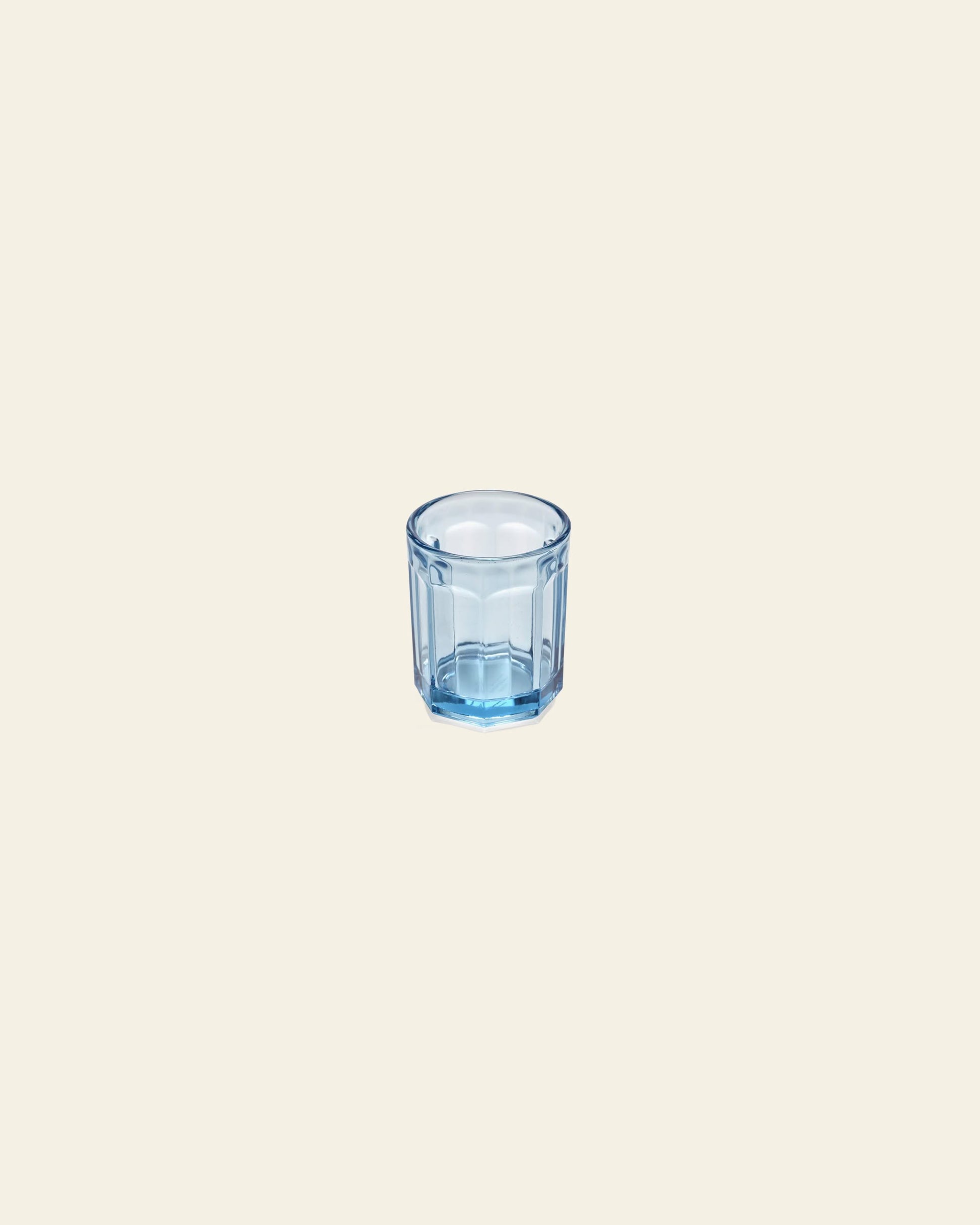 The Serax Fish & Fish Glass M, a small transparent blue glass cup with vertical ridges by Serax, is shown on a plain light beige background.