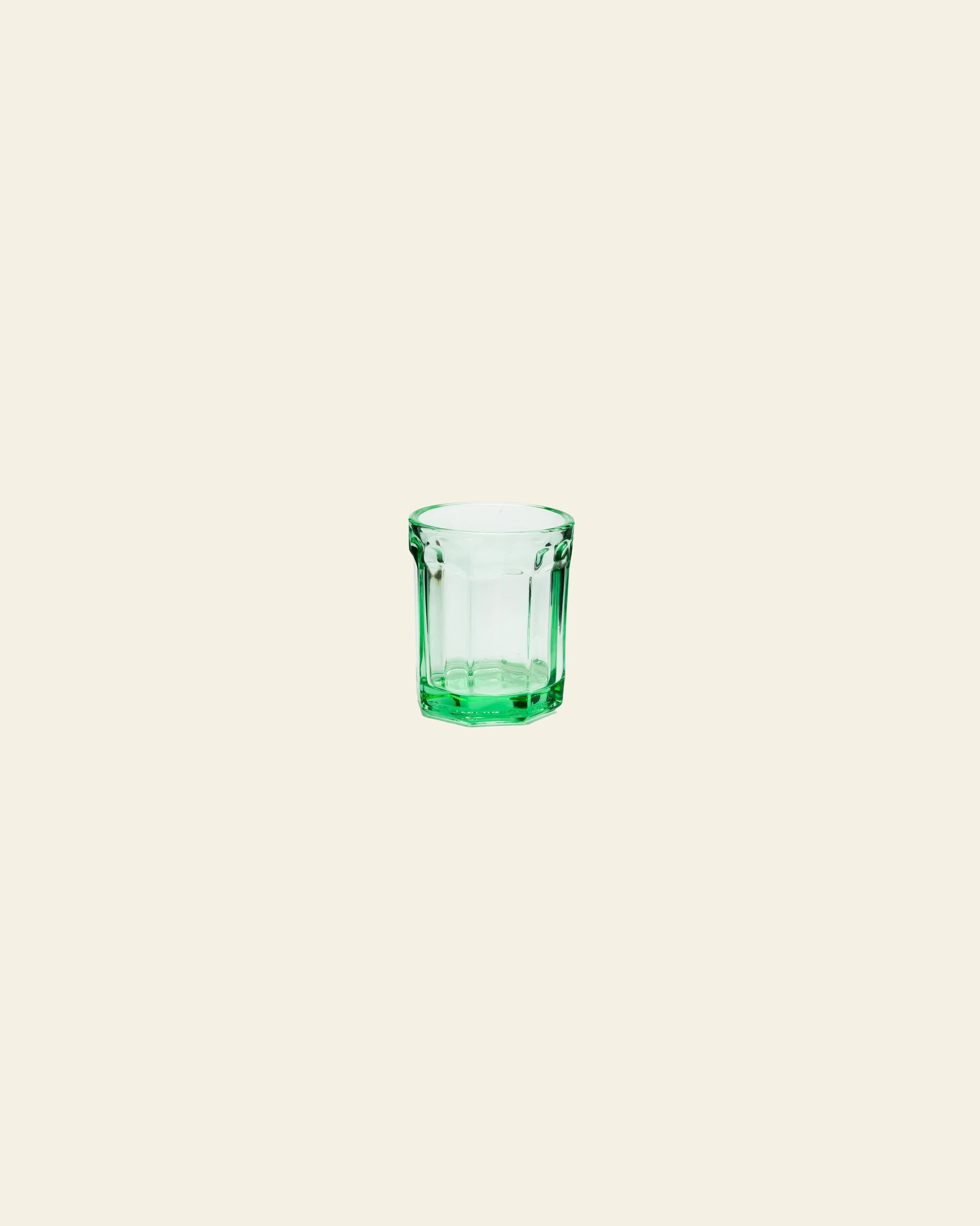 A small, empty Serax Fish & Fish Glass M in green is centered on a plain, light beige background.
