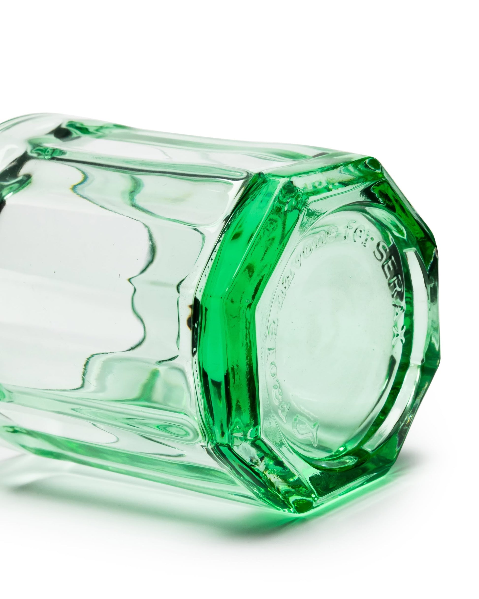 The Serax Fish & Fish Glass M - Green by Serax lies on its side, showing off its transparent green color, octagonal base, and smooth, faceted sides.