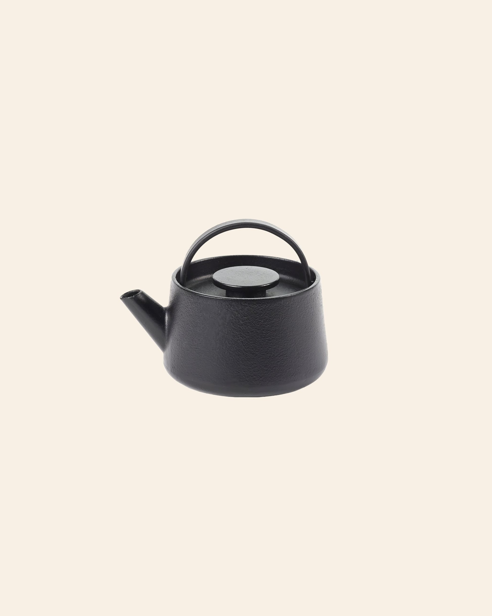 The Serax Inku Cast Iron Teapot S in black, featuring a curved handle and short spout, stands out against a light beige background, showcasing the brands understated elegance.