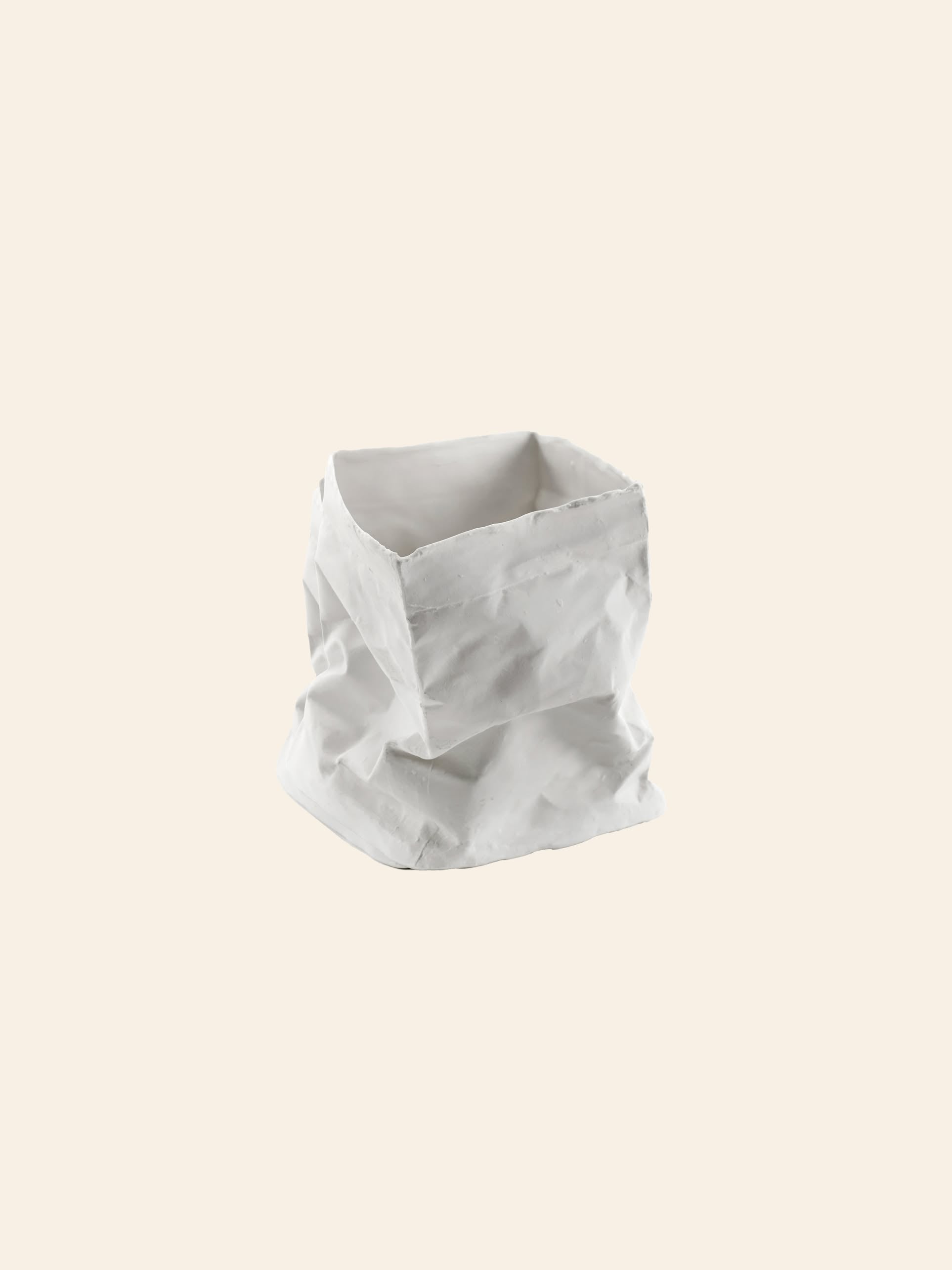 A white Serax Kiki Paperbag L, inspired by Dutch design, stands upright with a crumpled, square shape against a plain light beige background. The Serax bag appears empty and slightly wrinkled.