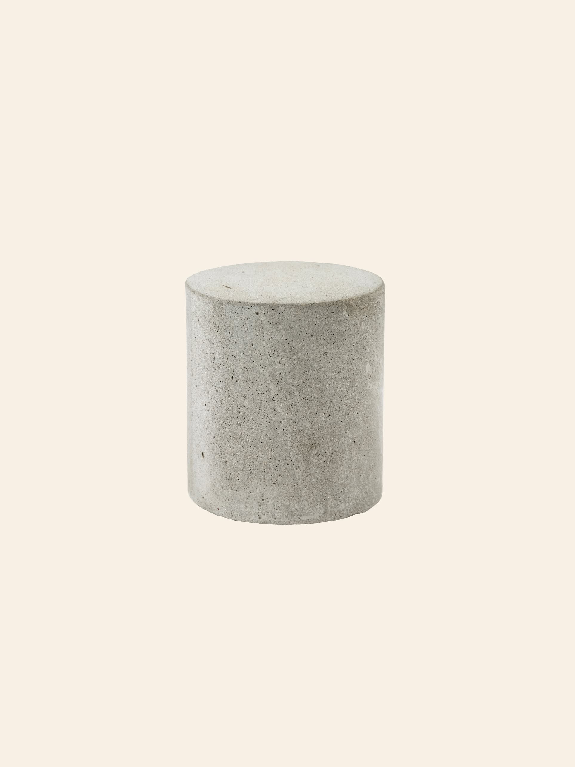 The Serax Marie Cylinder Concrete - Grey by Serax stands upright against a plain beige background, showcasing minimalist design with an industrial edge.
