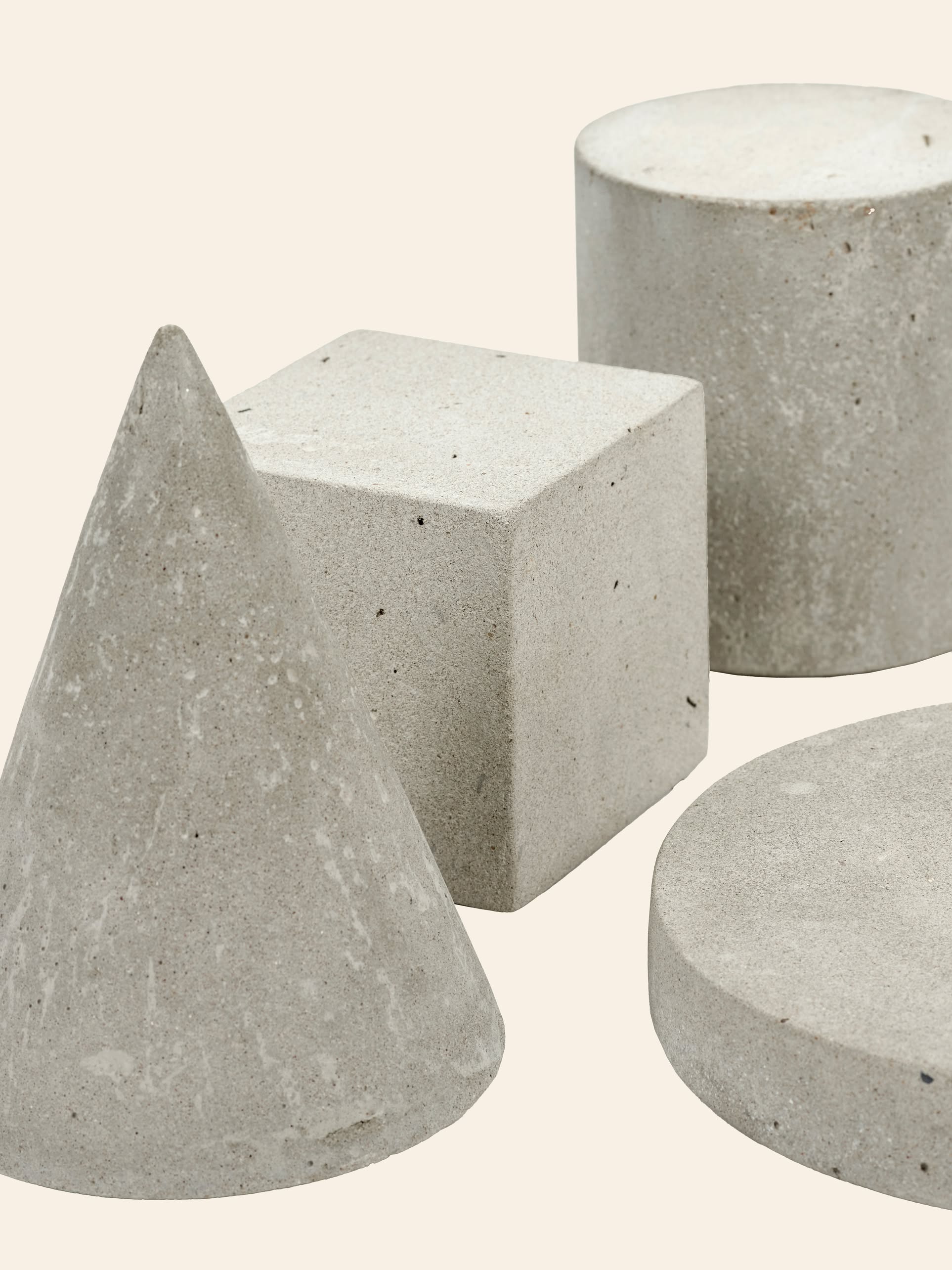 The Serax Marie Cylinder Concrete - Grey by Serax is shown with other concrete shapes on a neutral background. Its rough, speckled texture creates an industrial feel and emphasizes the minimalist design of the scene.