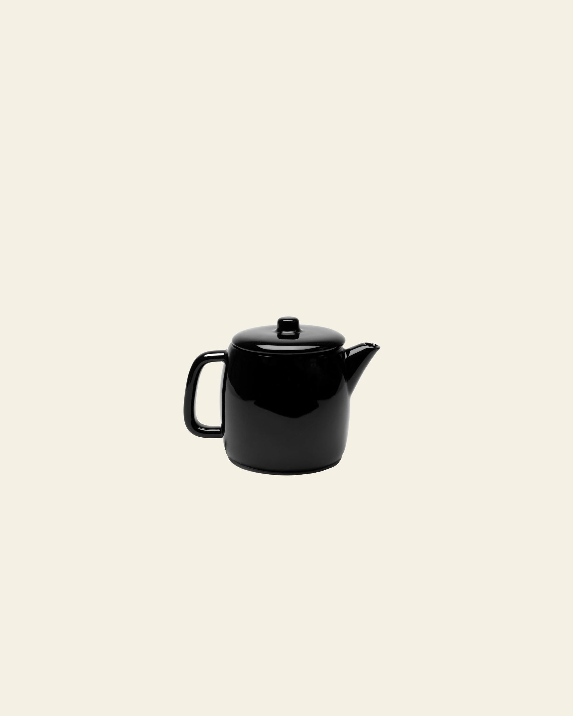The Serax Passe-Partout Teapot in glossy black porcelain, by Serax, features a minimalist design with a handle and spout, elegantly centered on a light beige background.