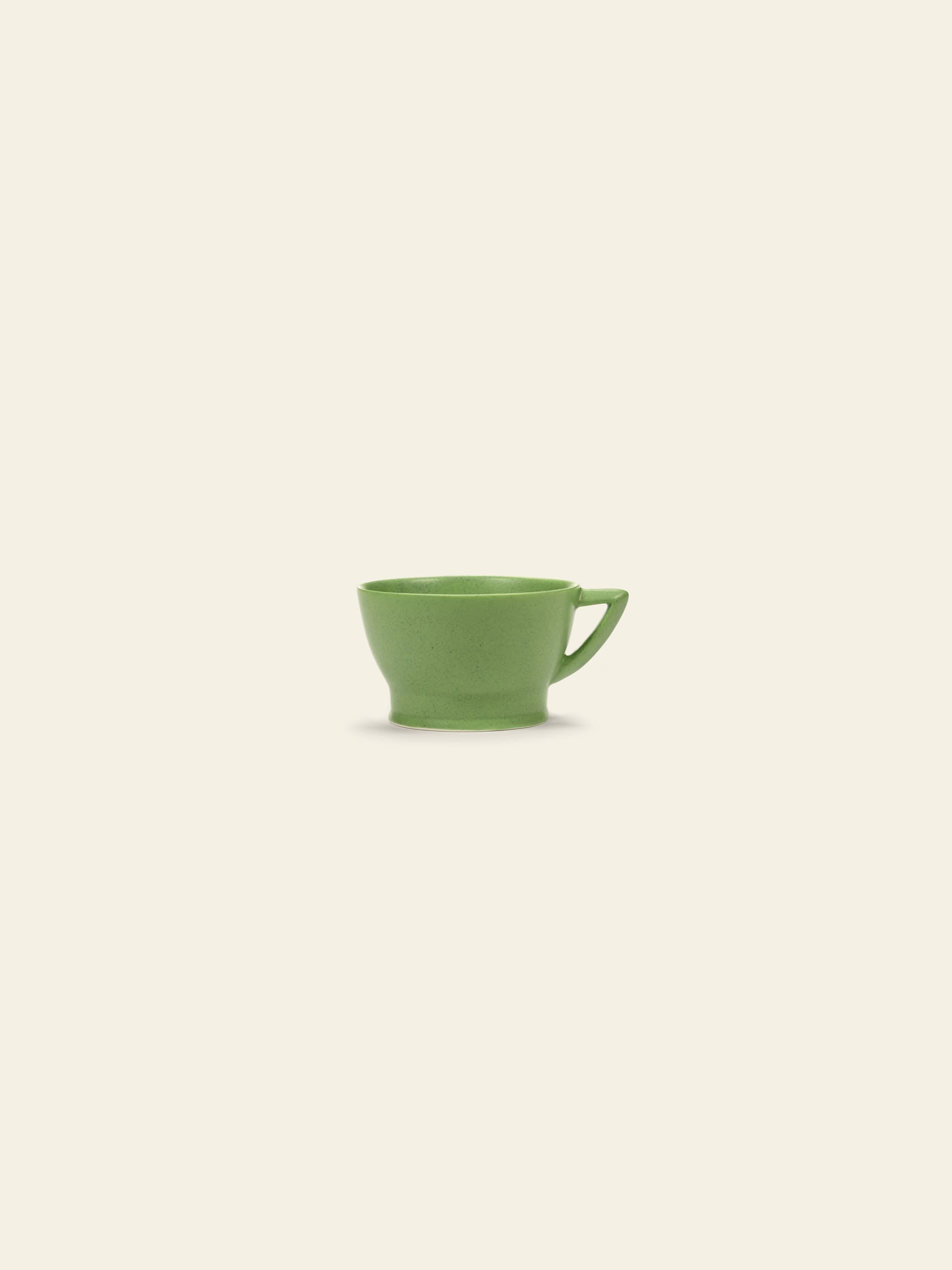 The Serax Ra Cup - Green, a small porcelain cup with a handle inspired by Ann Demeulemeester tableware, is centered on a plain light beige background.