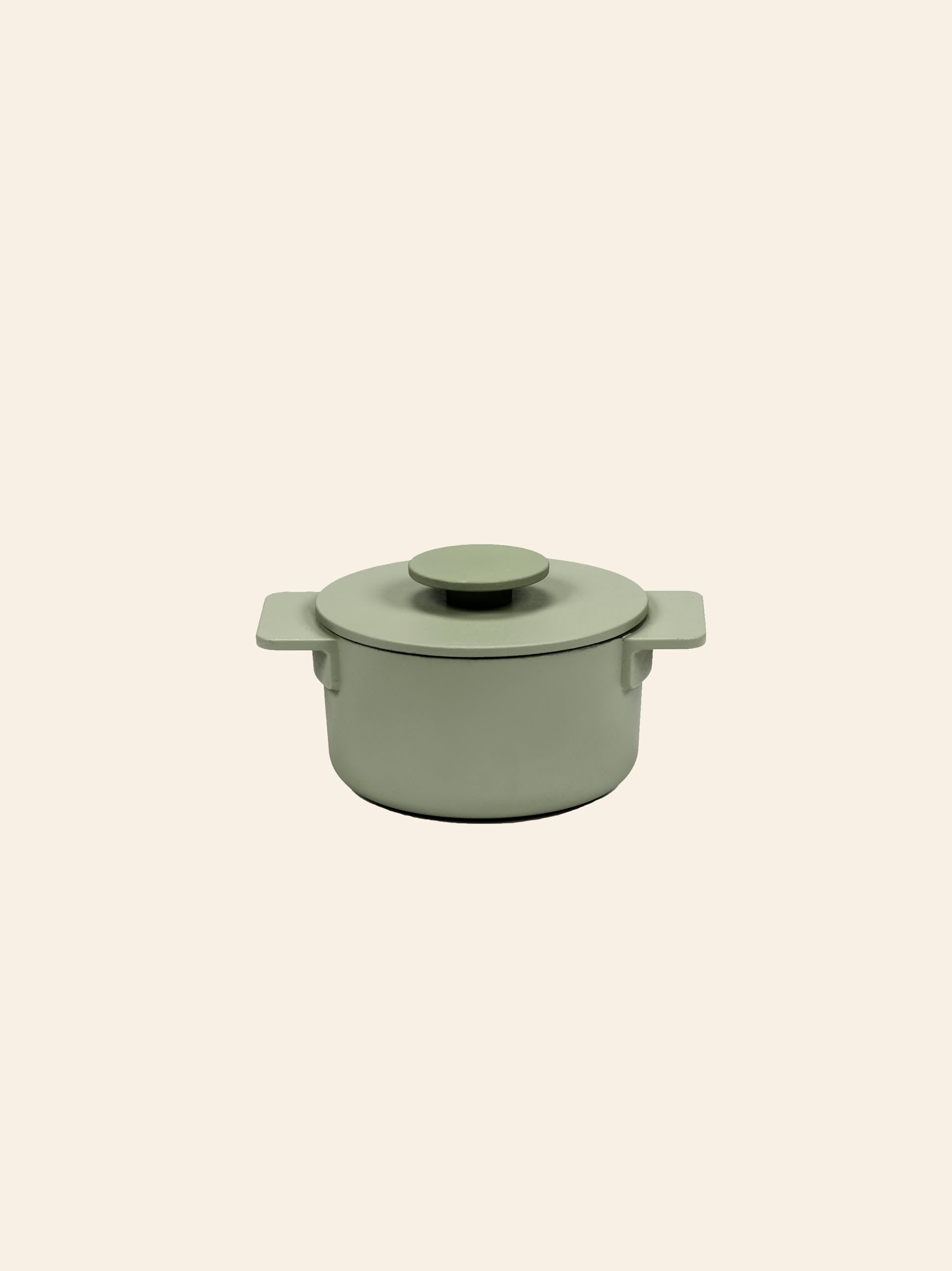 The Serax Surface Cast Iron Pot XS in camogreen, featuring a round shape, lid, and two side handles, is centered on a plain beige background.