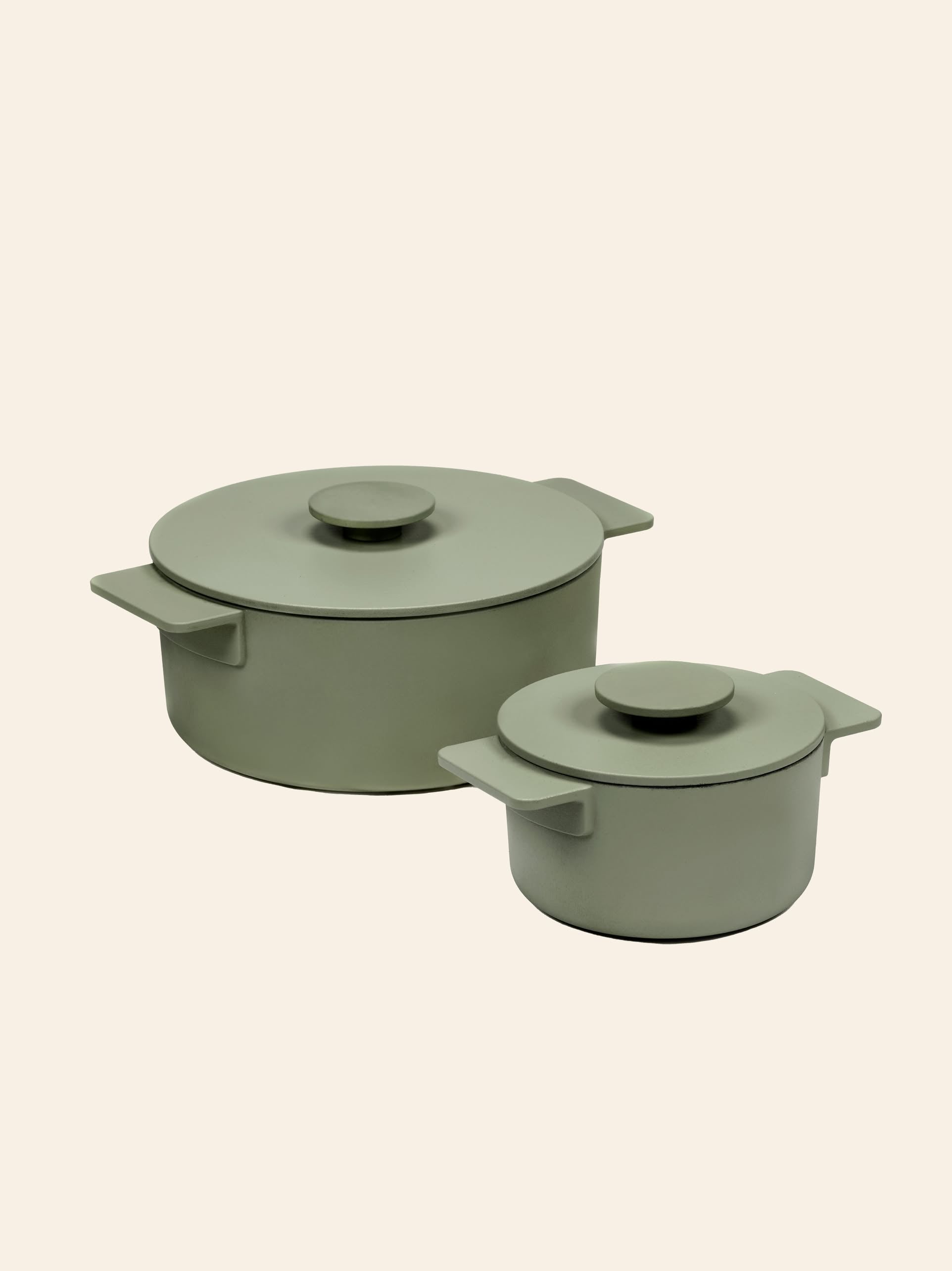 Two Serax Surface Cast Iron Pots XS in Camogreen sit side by side on a neutral background; these stylish sage green pots with matching lids add timeless charm and are perfect for cooking in any kitchen.