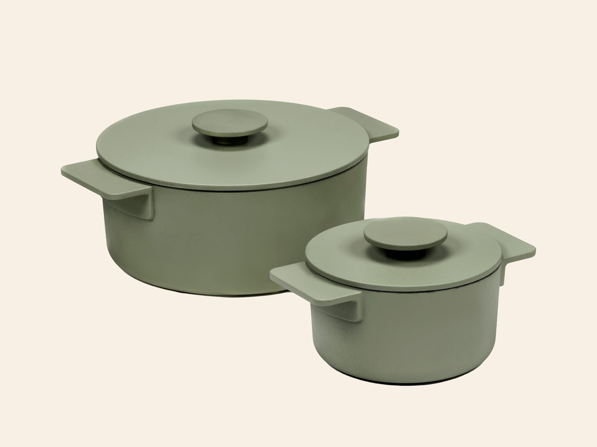 Two Serax Surface Cast Iron Pots XS in Camogreen with matching lids and handles—one large, one small—feature a matte finish. Displayed on a beige background, they’re perfect for any kitchen and ideal for all your cooking needs.