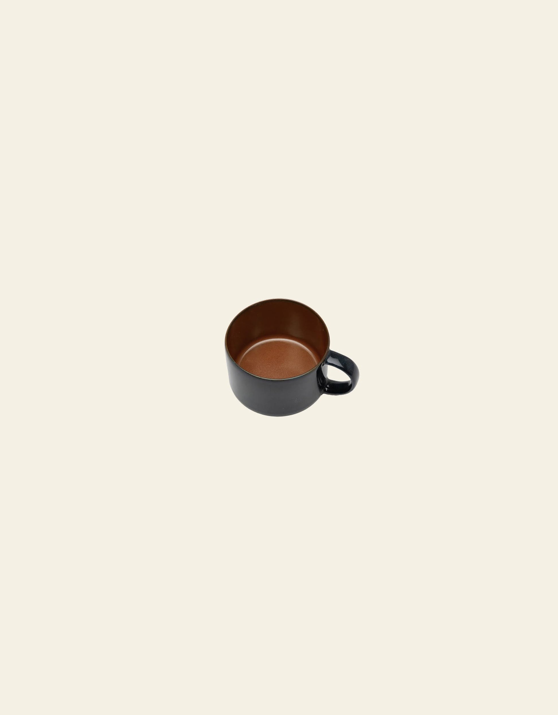 The Serax Terres De Rêves Coffee Cup by Serax features handcrafted black stoneware with a brown interior and a handle, showcased on a plain light beige background.